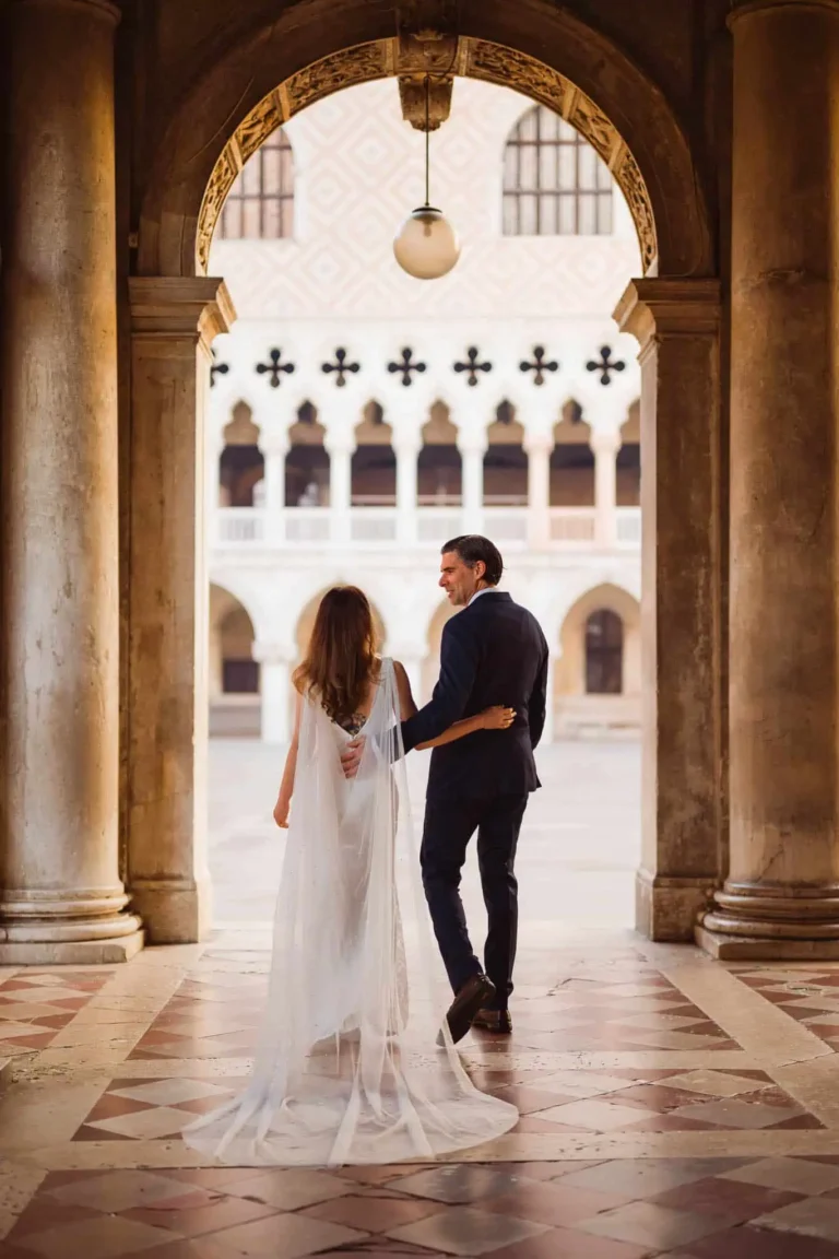 1. Elegant bride and groom walking through Venice palace archway, romantic wedding scene.