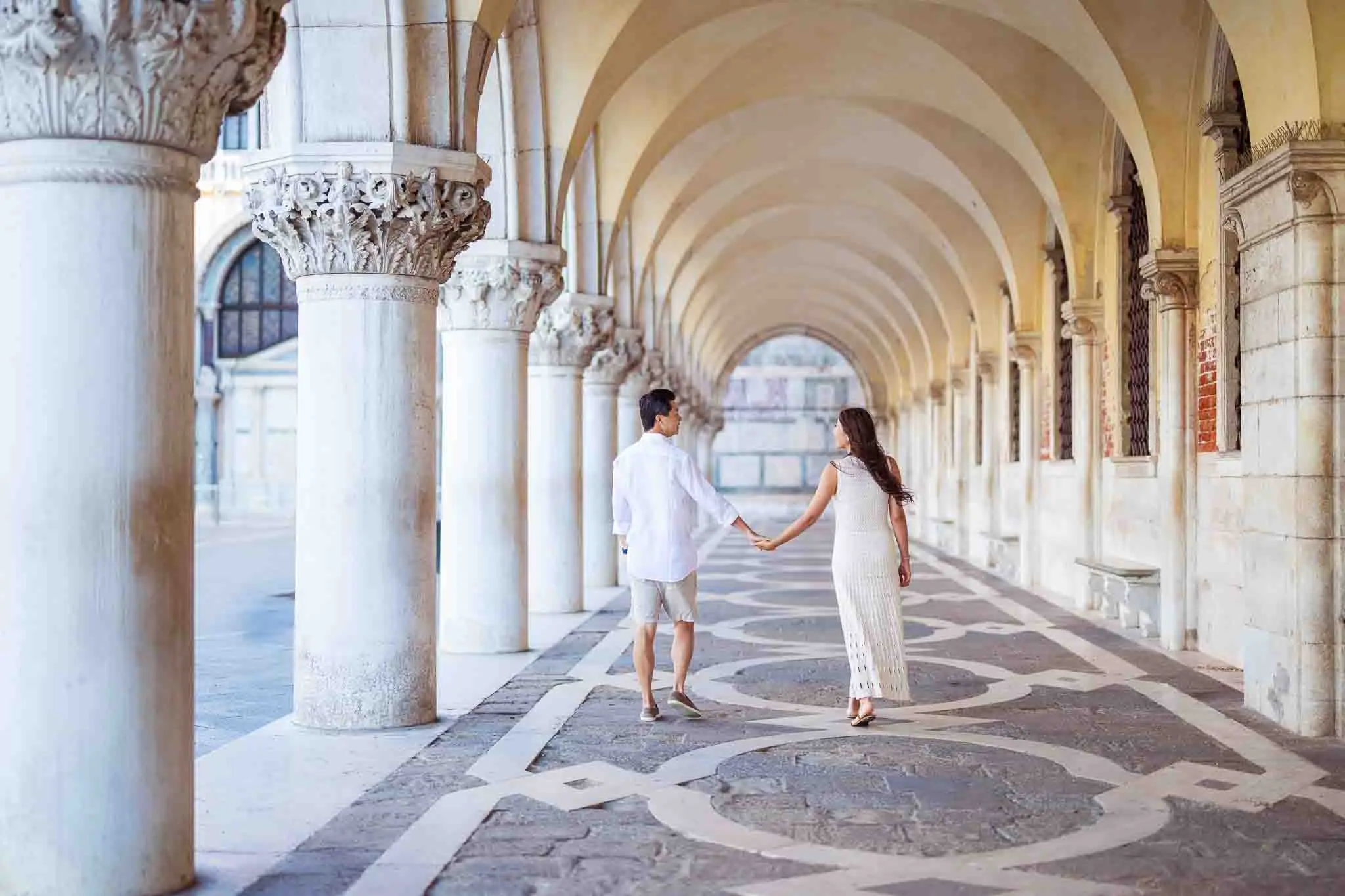 Elegant couple holding hands in Venice archway, romantic wedding proposal photography.