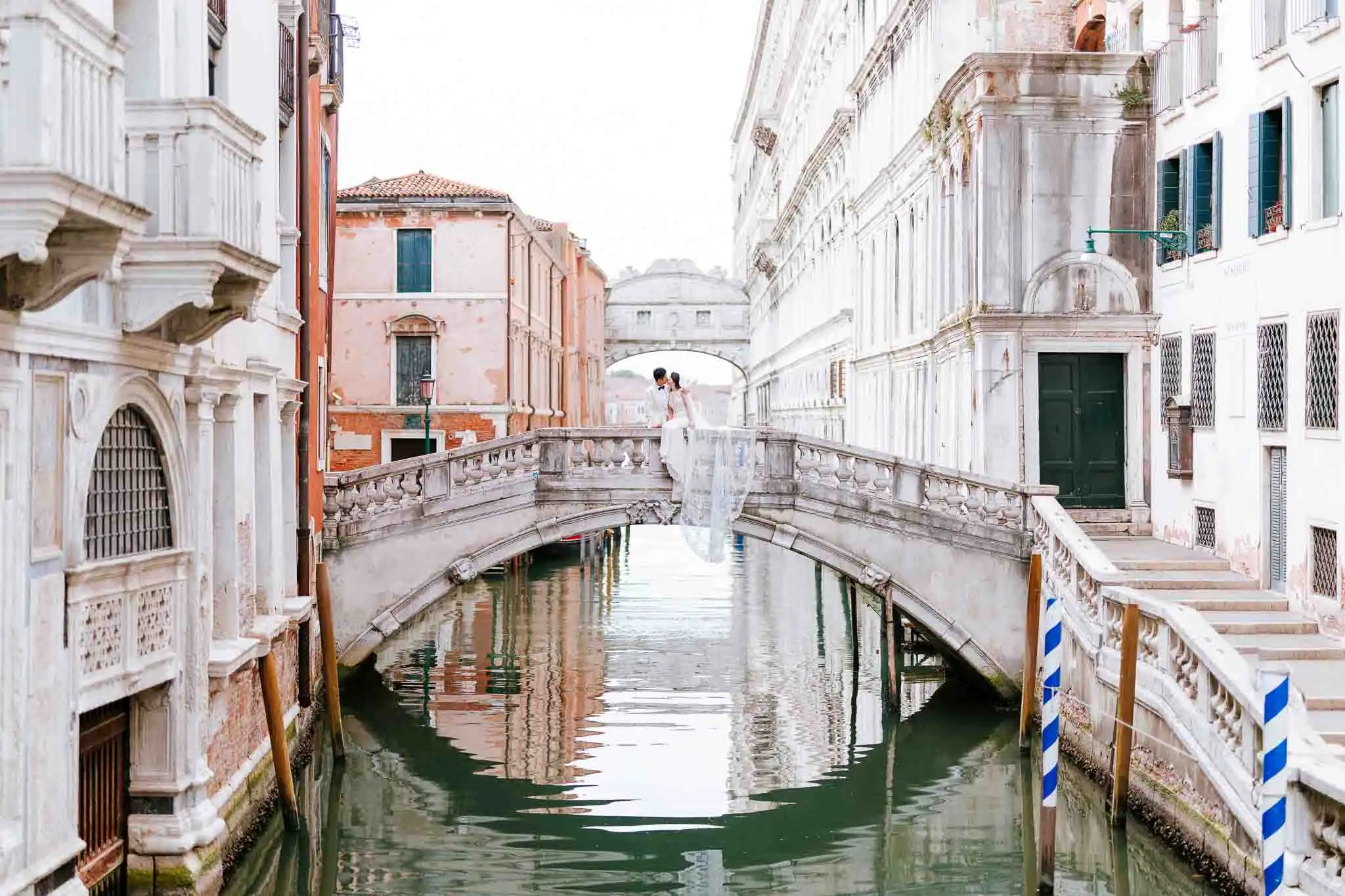 Elegant wedding couple sharing a romantic moment on a Venetian bridge, surrounded by historic architecture and serene canal waters.