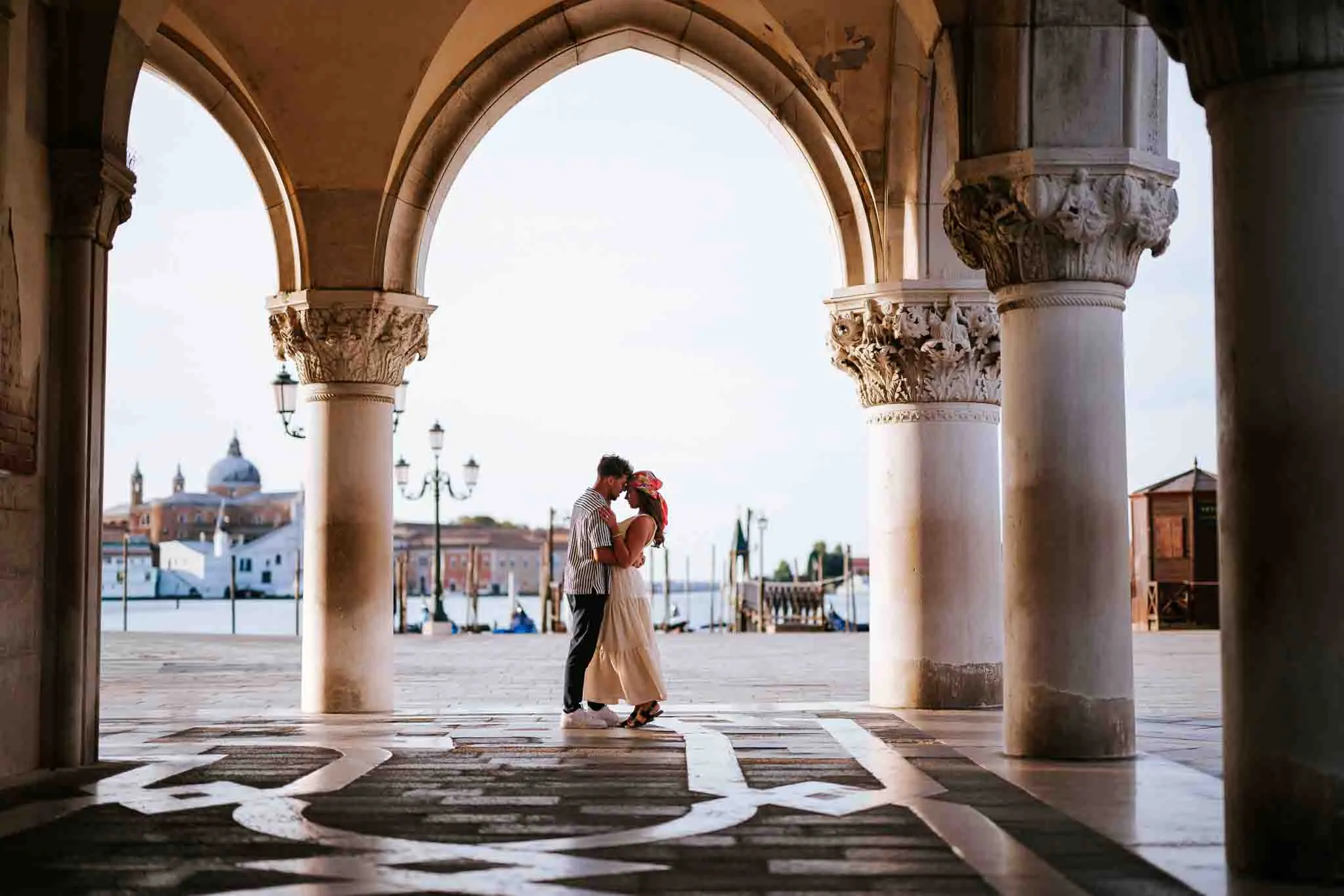 Romantic Couple Photoshoot in Venice embracing under Venetian arches at sunset.