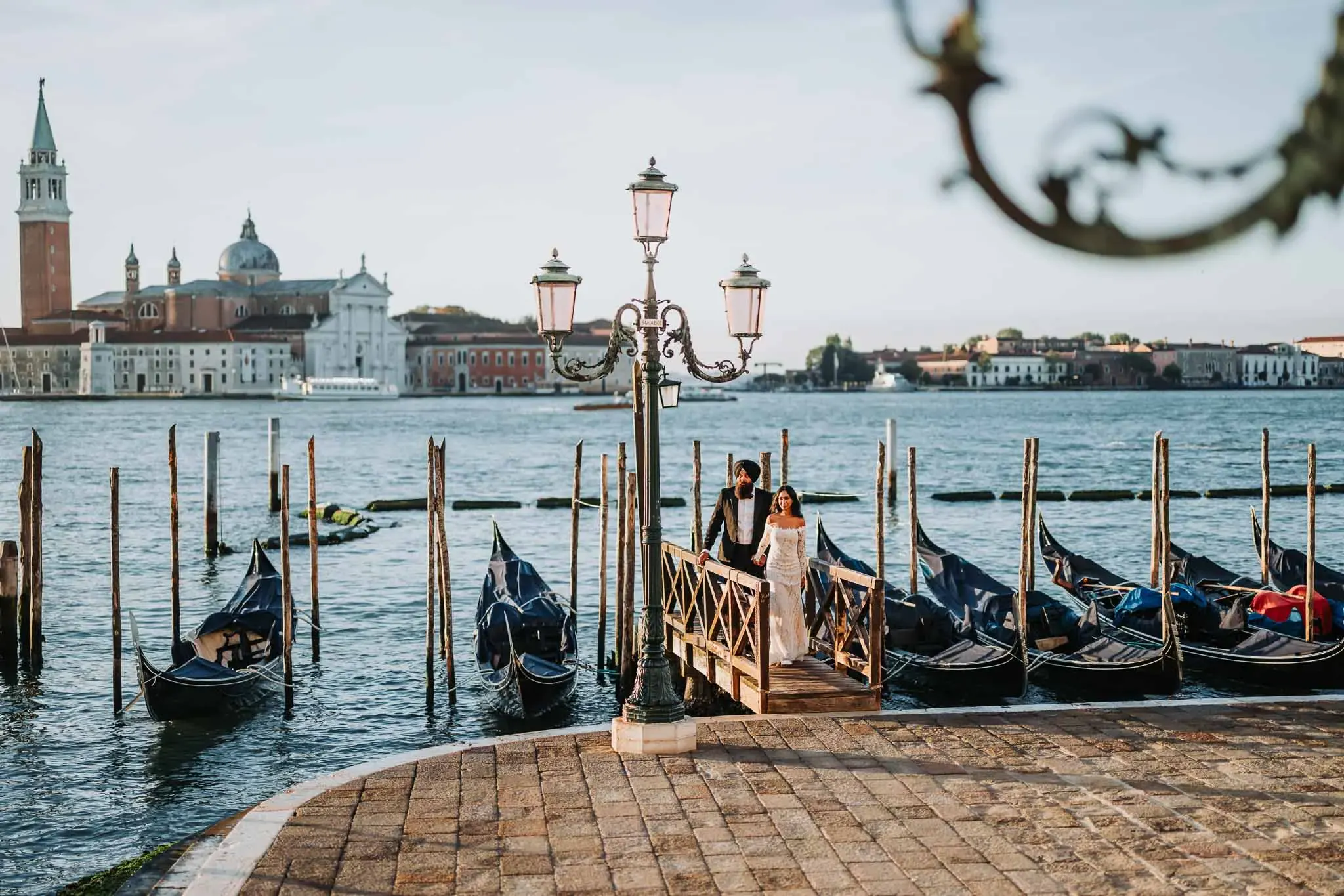 Gondola dock in Venice with a couple in wedding attire, scenic cityscape and iconic architecture in background.