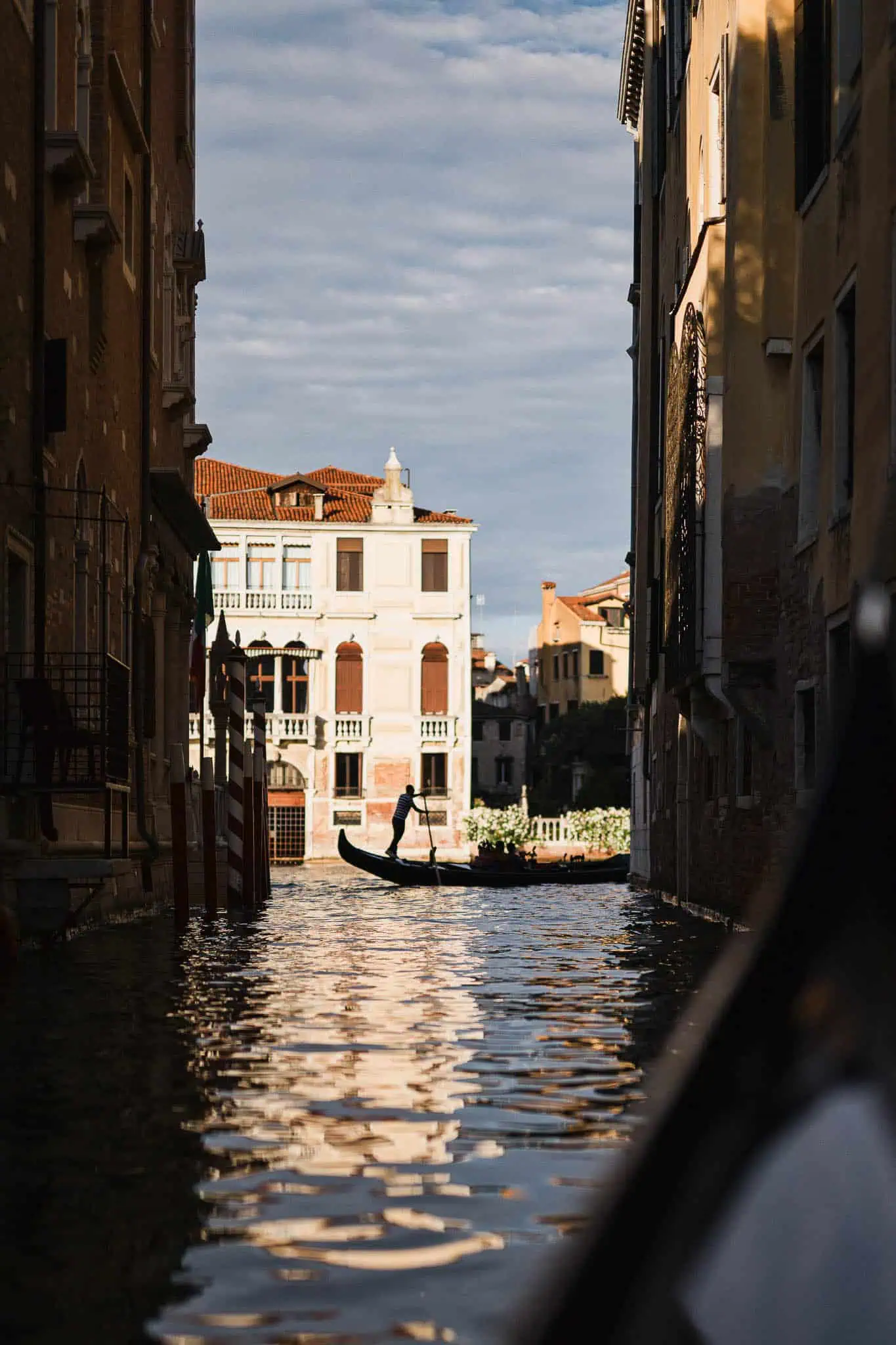 Gondola navigating Venice canals at sunset, with historic buildings and blue sky.