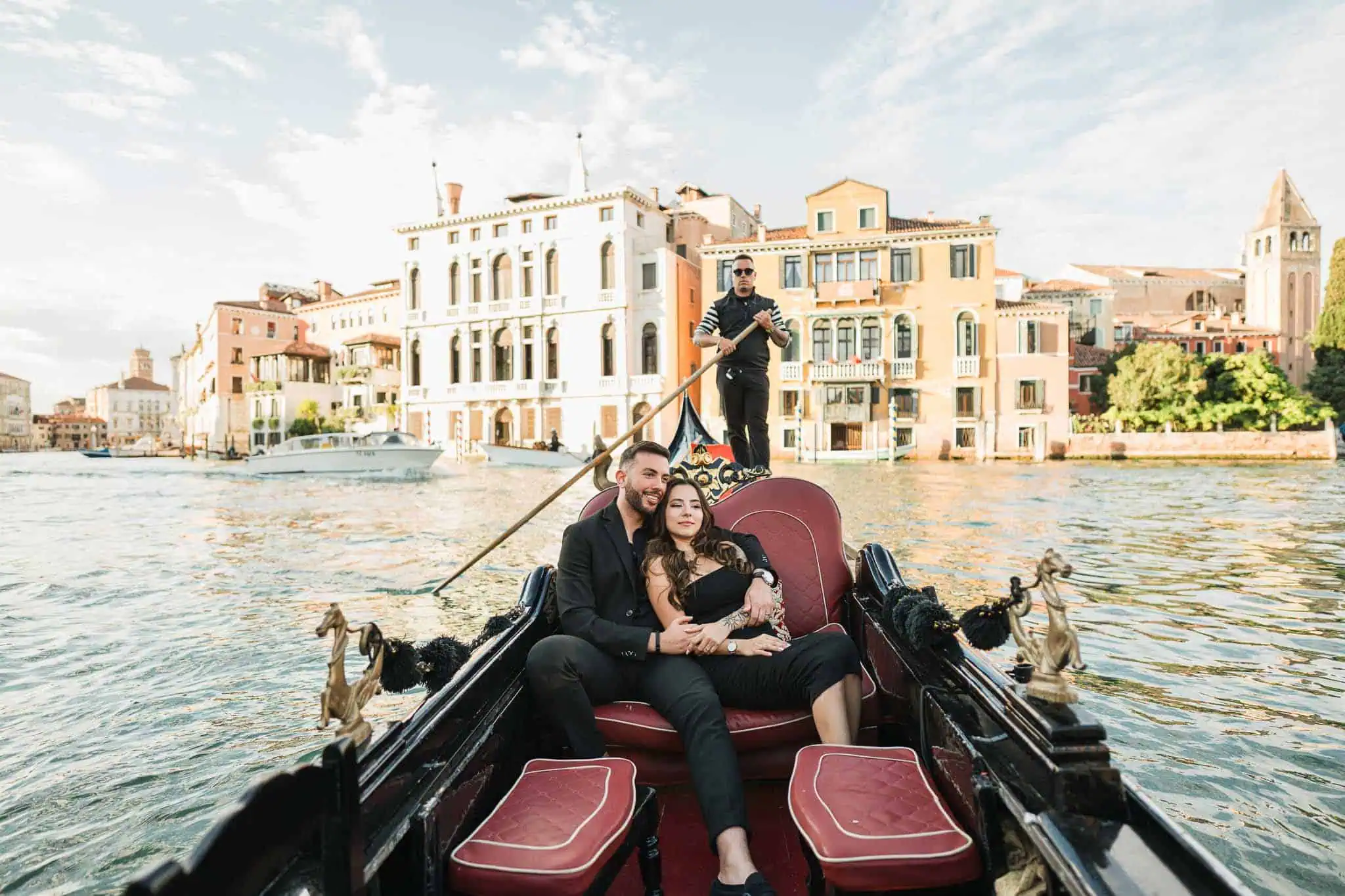 Romantic couple on gondola ride in Venice with historic buildings in background.
