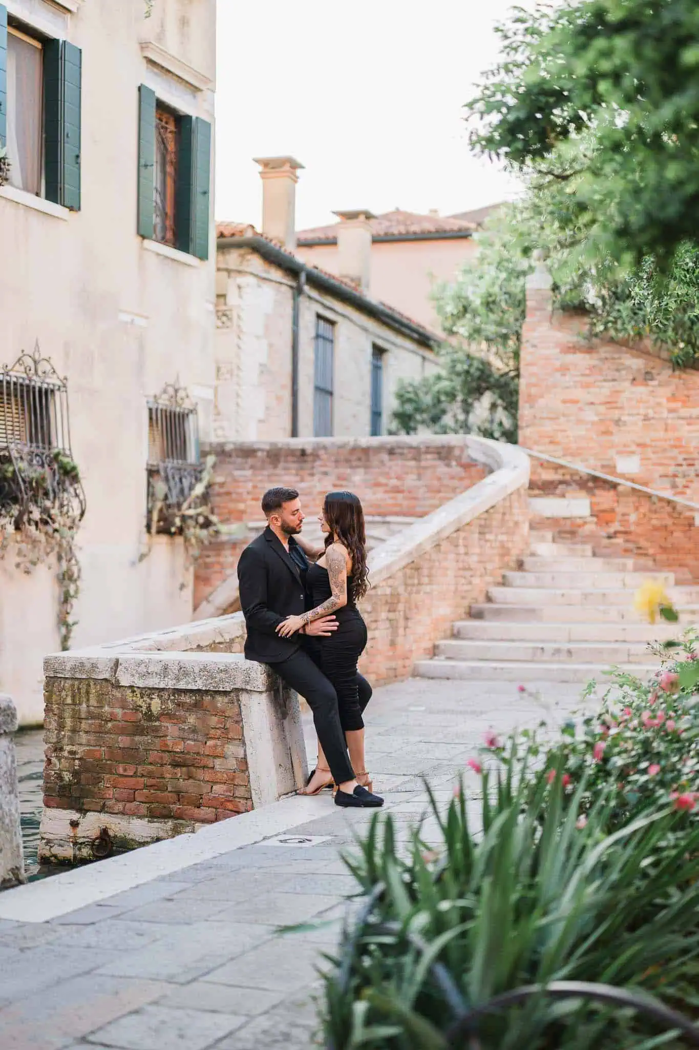 Romantic couple in Venice with historic buildings and colorful gardens in the background.