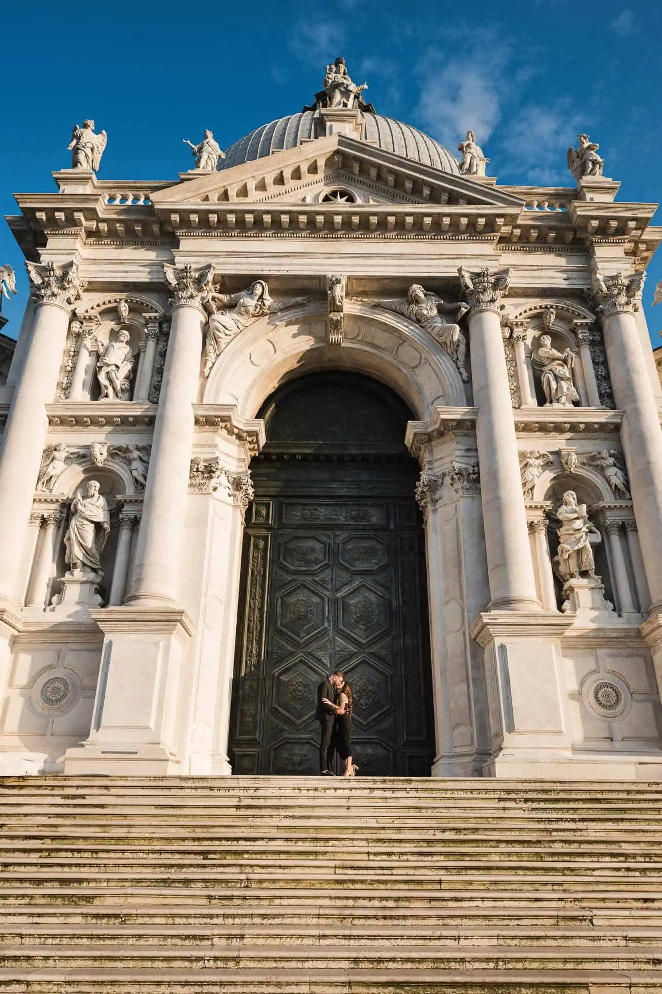Elegant couple kissing in front of historic Venice cathedral, capturing romantic wedding, proposal, engagement moments.