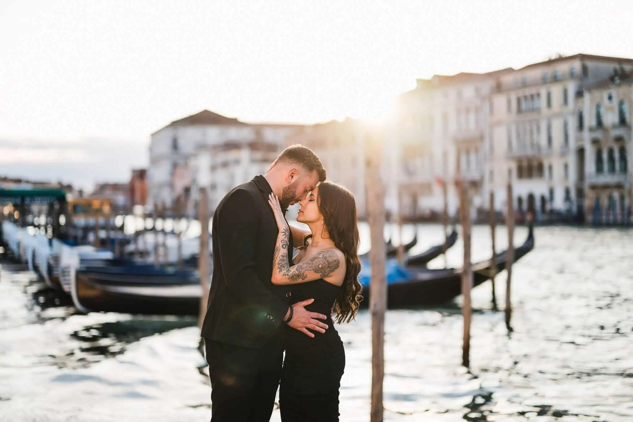 Romantic Venice engagement photo with couple kissing at sunset near gondolas and historic buildings.