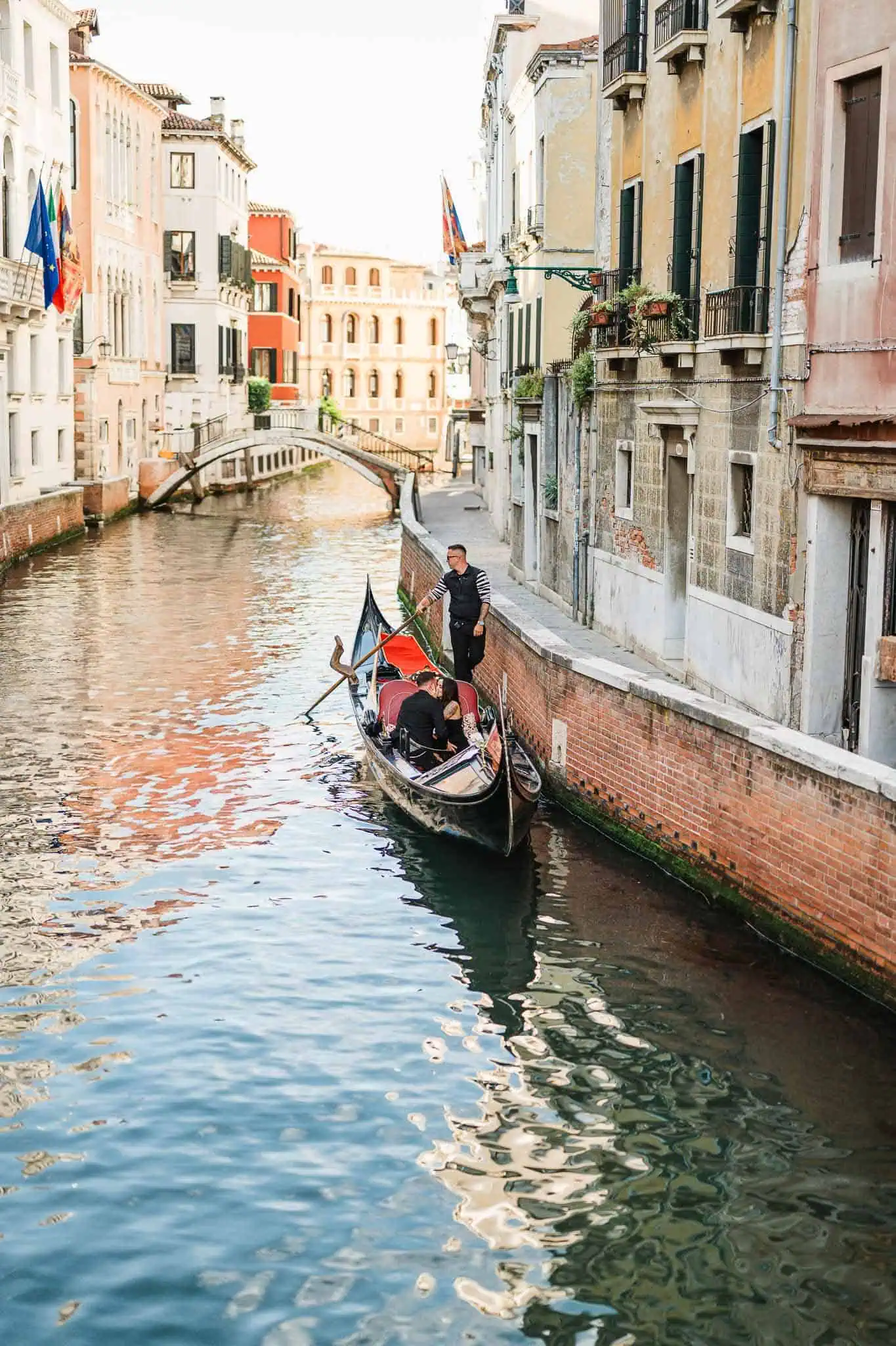 Gondola ride along Venice canal with historic buildings and distant bridge in the background.