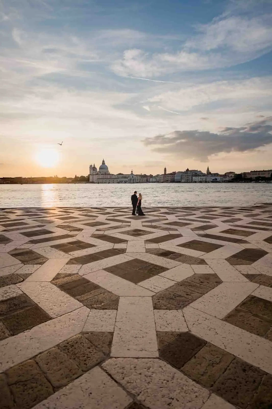 Romantic couple walking at sunset on Venice waterfront, overlooking iconic city skyline.