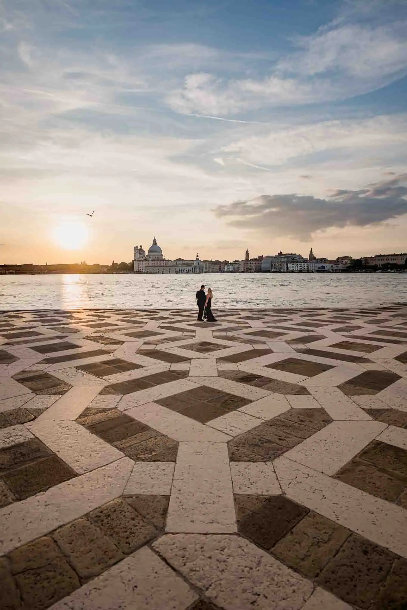 Romantic couple walking at sunset on Venice waterfront, overlooking iconic city skyline.