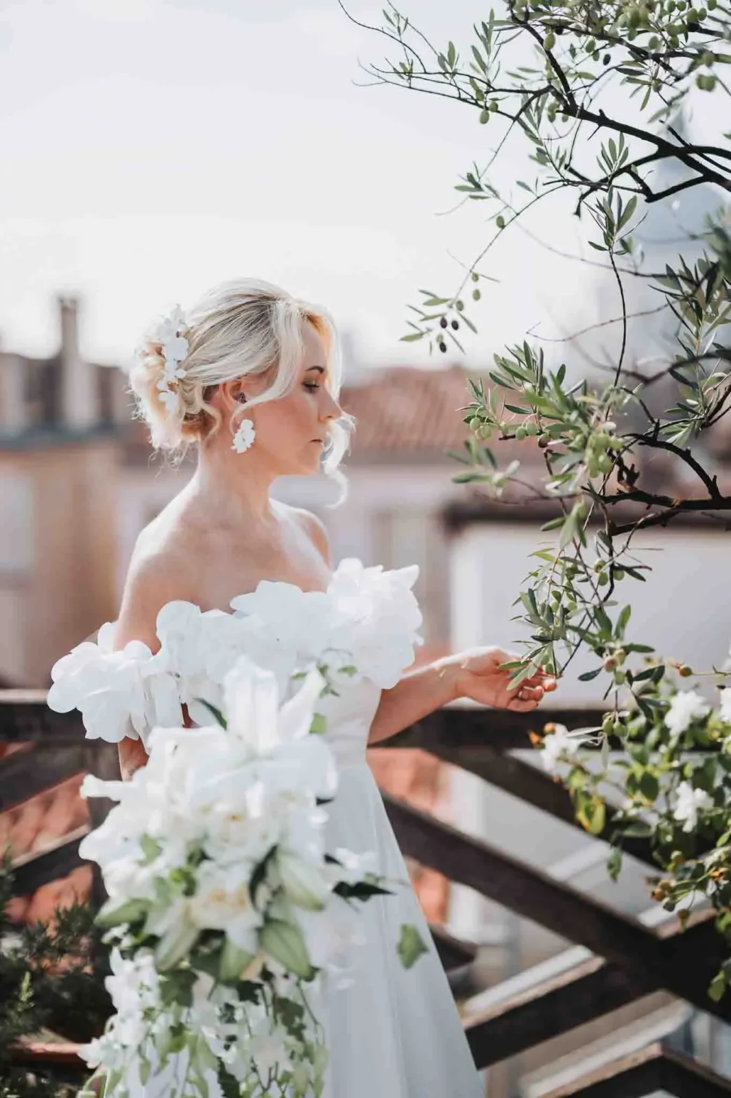 Elegant bride in white wedding gown with floral accessories, posed amidst greenery for romantic Venice wedding photos.