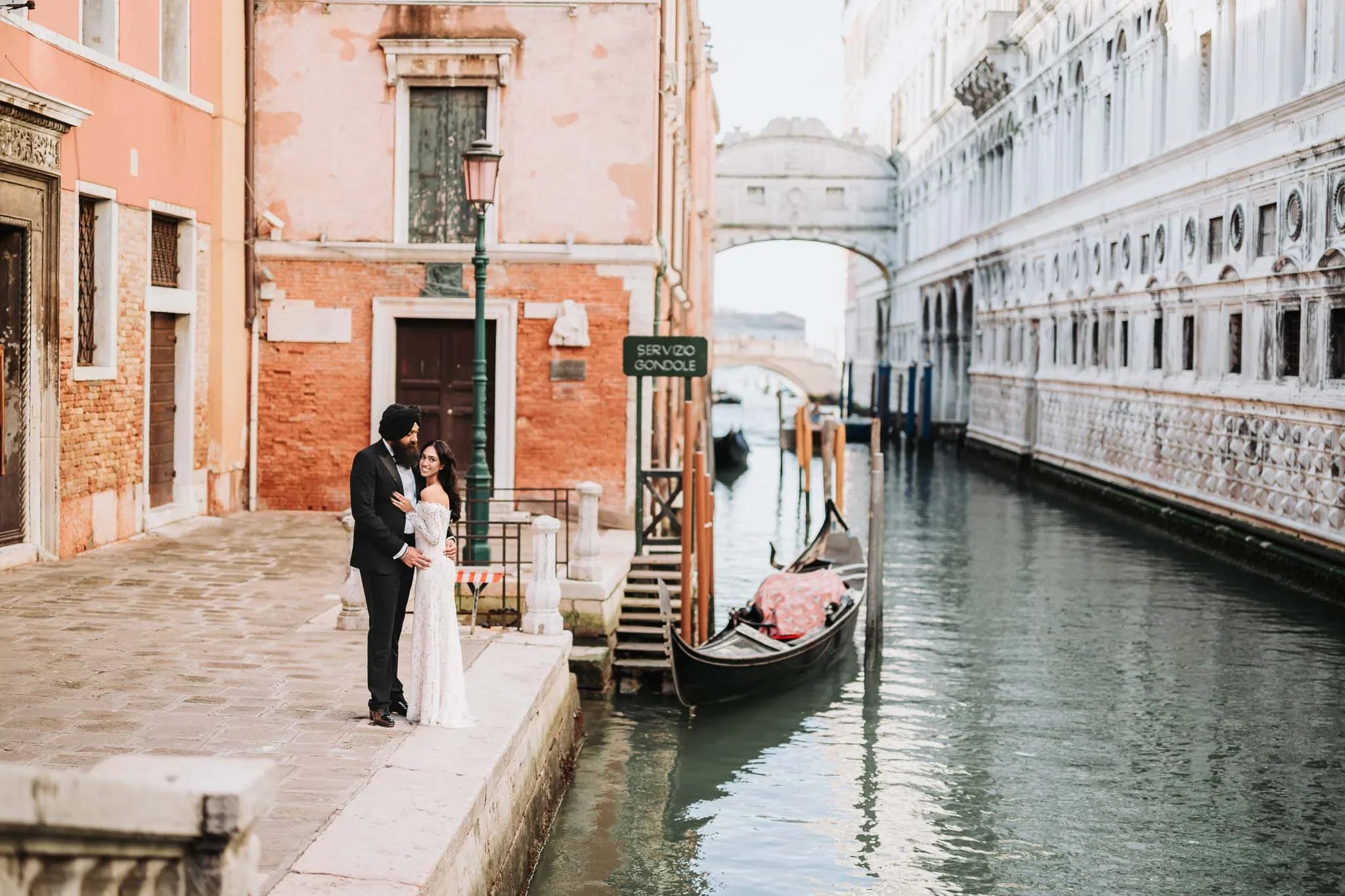 Romantic couple in Venice next to canal with gondola and historic buildings.