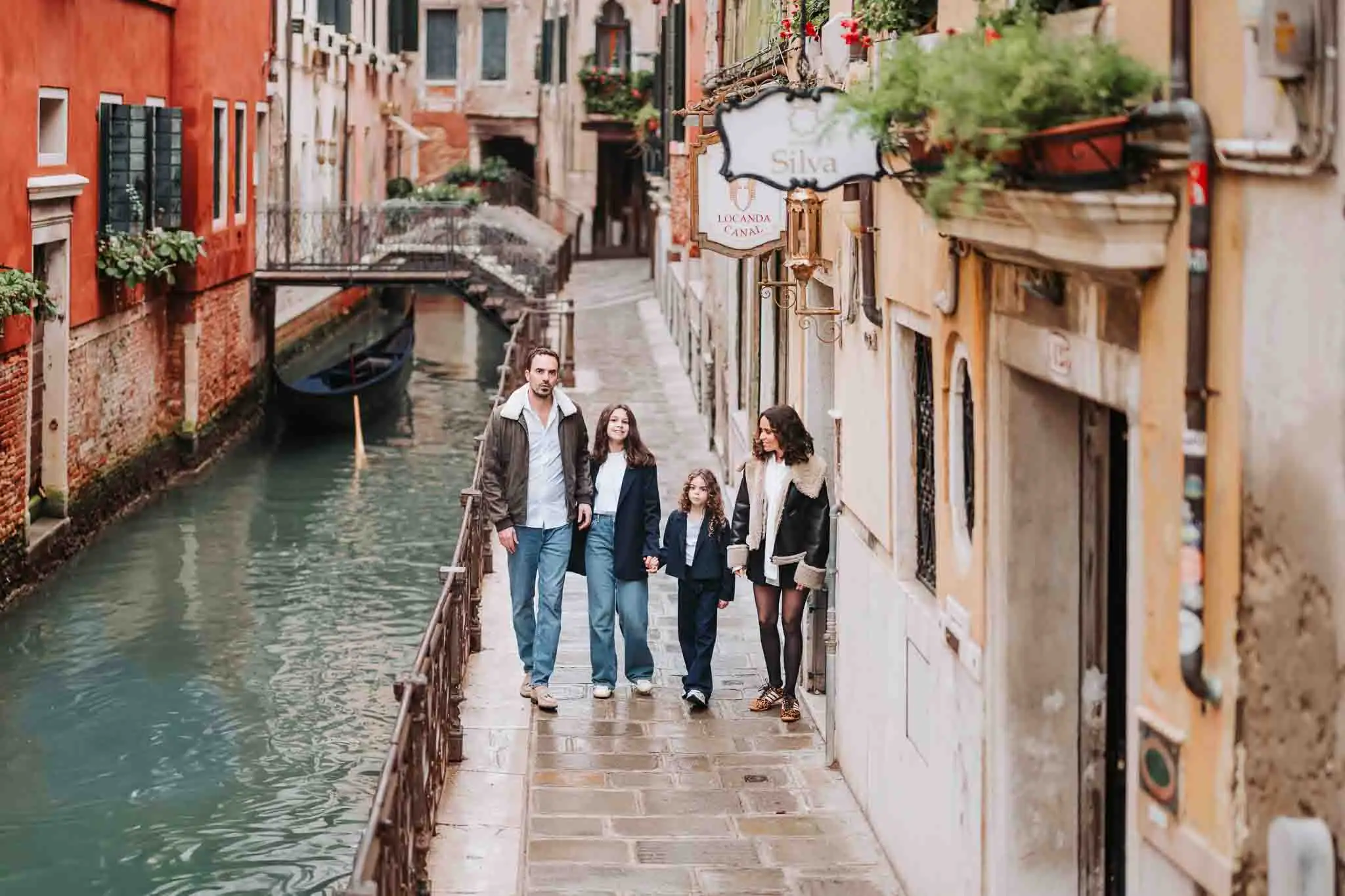 Charming family walking along a Venice canal, picturesque alley with colorful buildings, classic gondola in background.