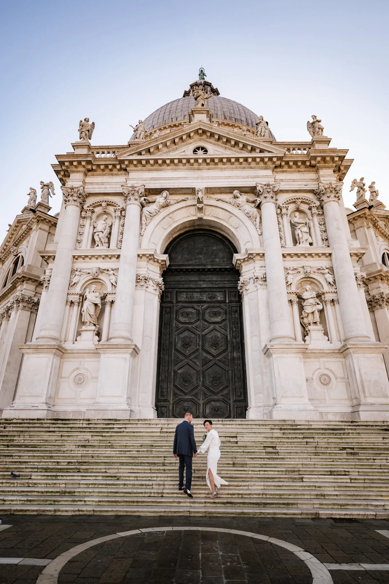 Elegant couple holding hands at Venice church steps, romantic wedding photo in Italy.