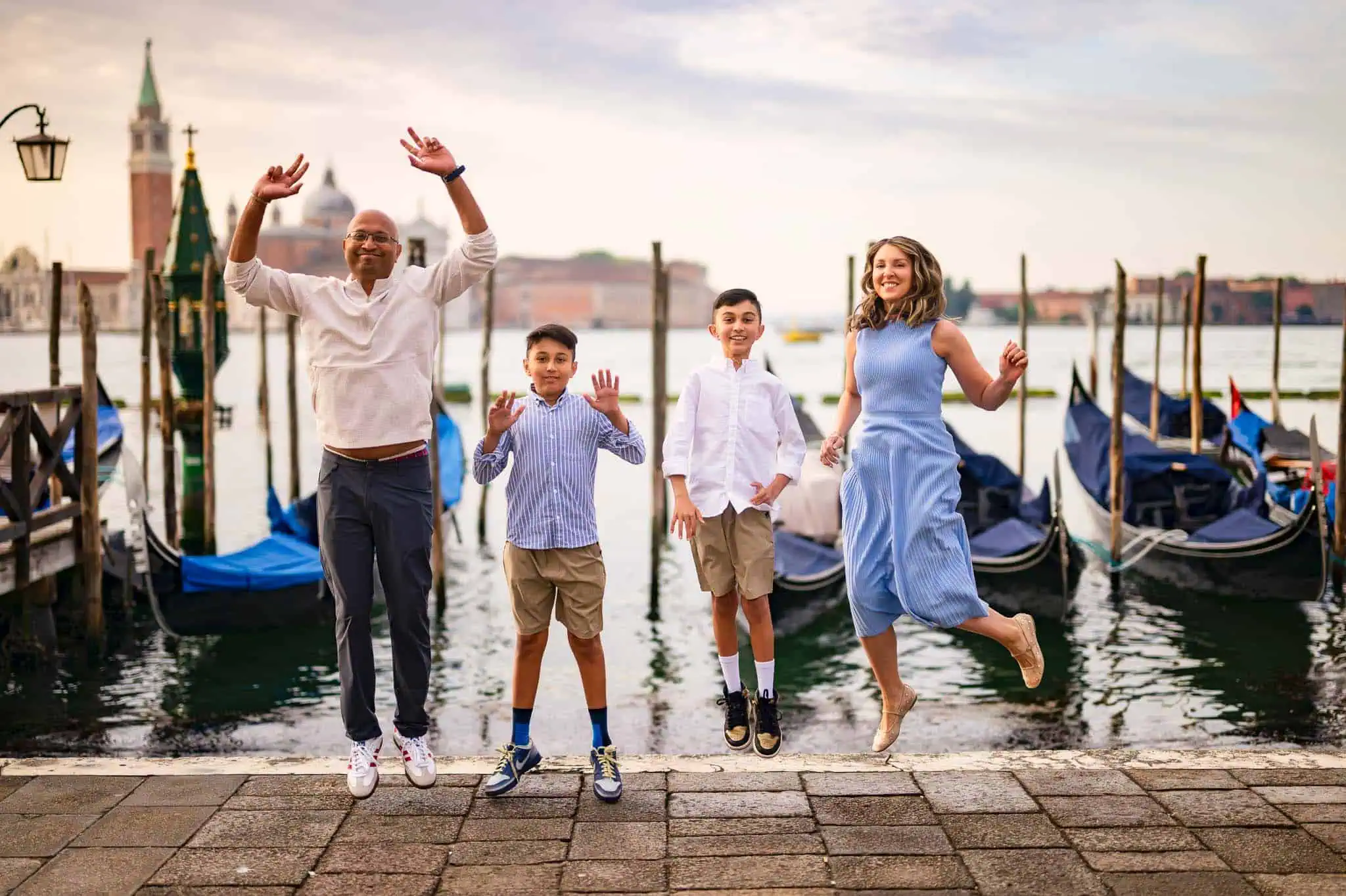 Venezian family jumping by gondolas with iconic architecture in background.