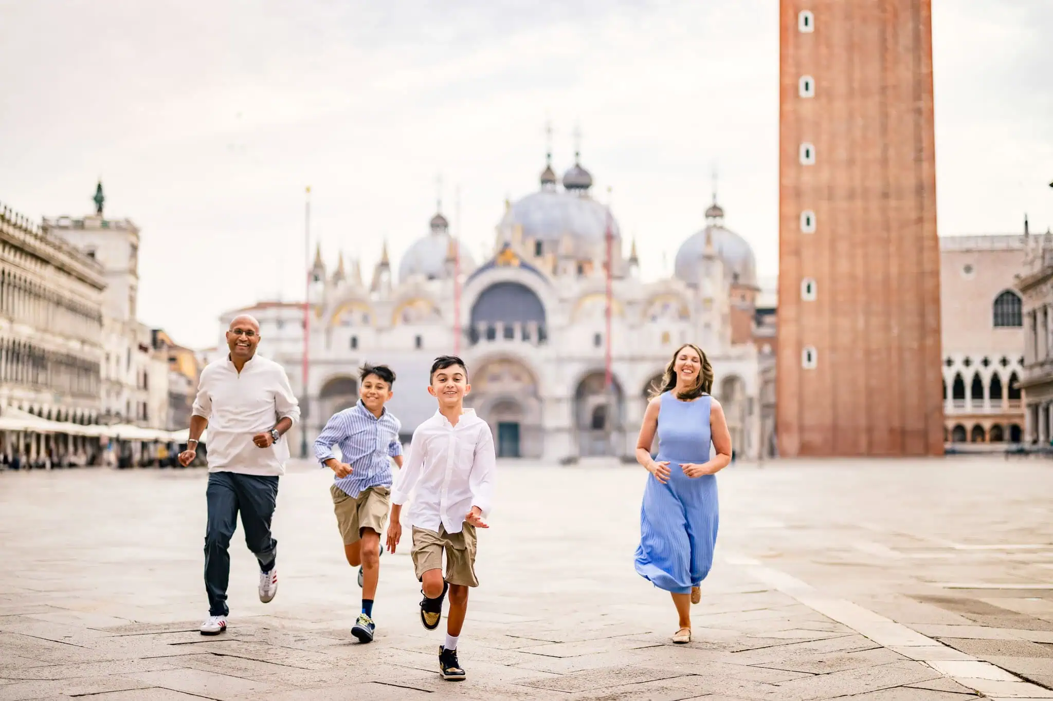 Happy family running in Piazza San Marco, Venice with the Basilica and Campanile in background.