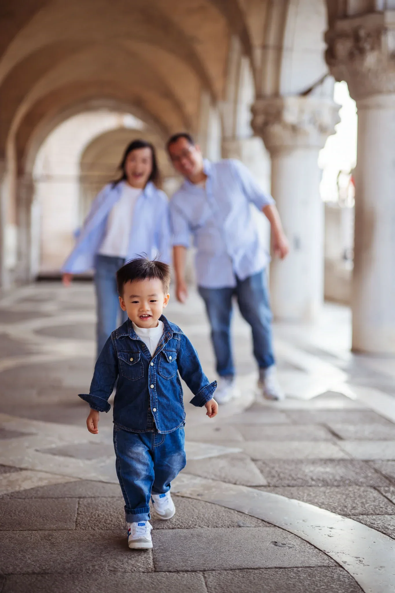 1. Smiling young boy walking in Venice historical arches with family in background.