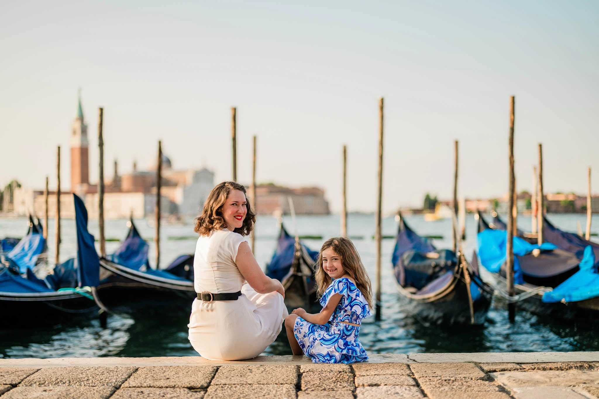 Gondola dock with women and girl enjoying Venice waterfront at sunset, travel photography, romantic cityscape, Italy.