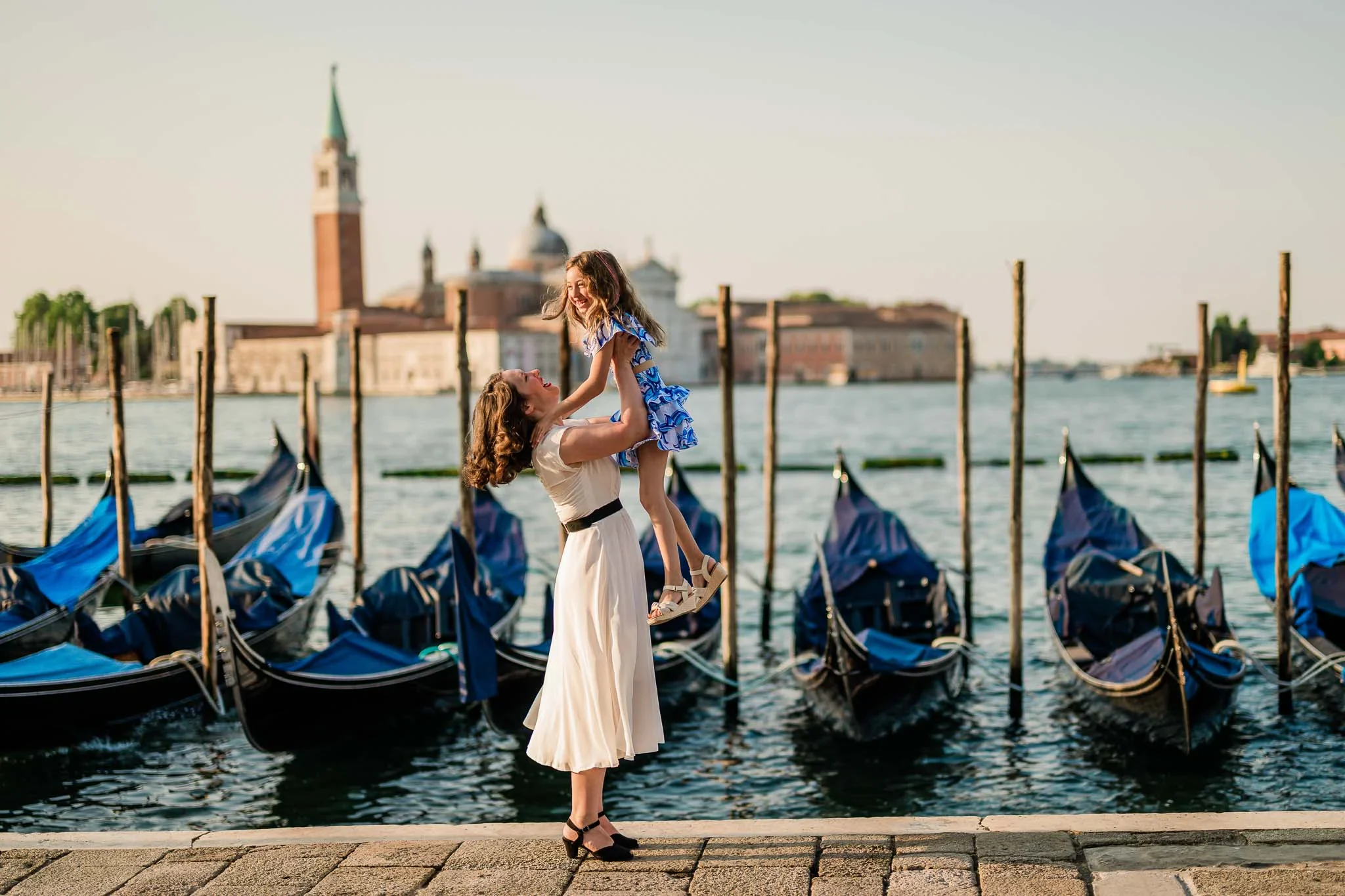 Venezian mother and daughter enjoying a joyful moment by the gondolas at sunset in Venice.