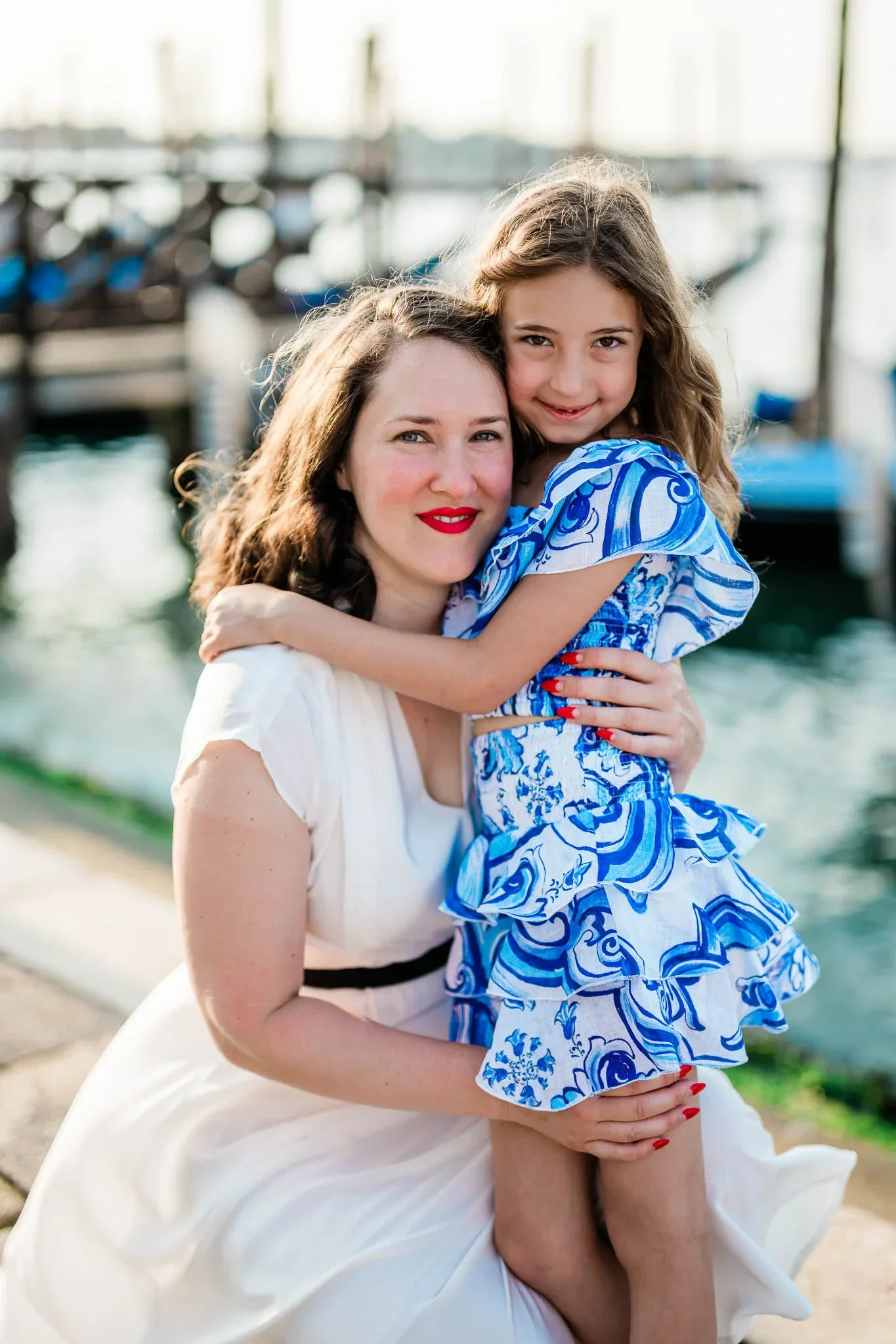 Joyful mother and daughter embracing by the Venice canal during a sunny day, capturing beautiful family moments in Italy.