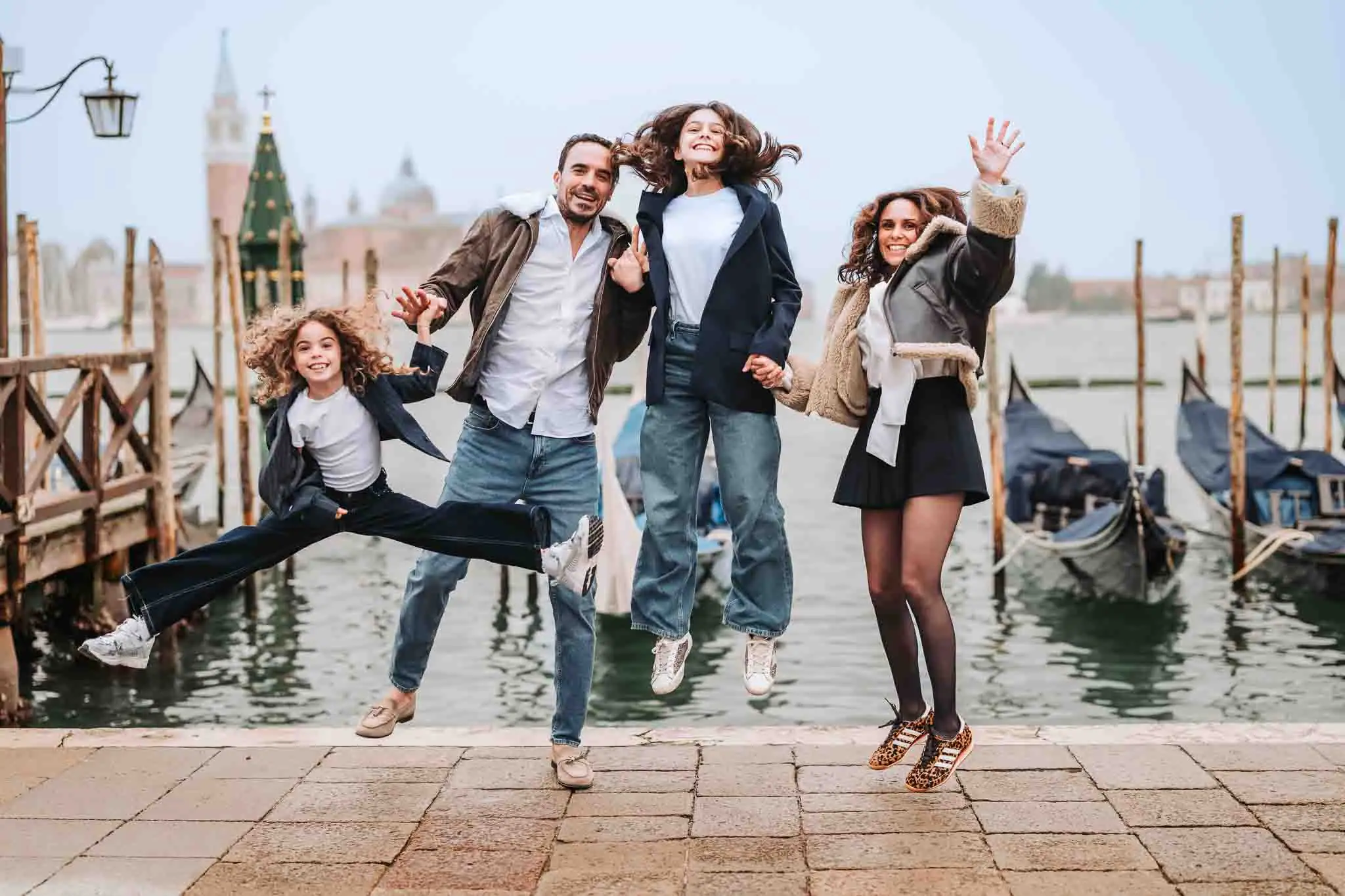 Joyful family jumping in Venice, Italy with gondolas and historic architecture in the background.