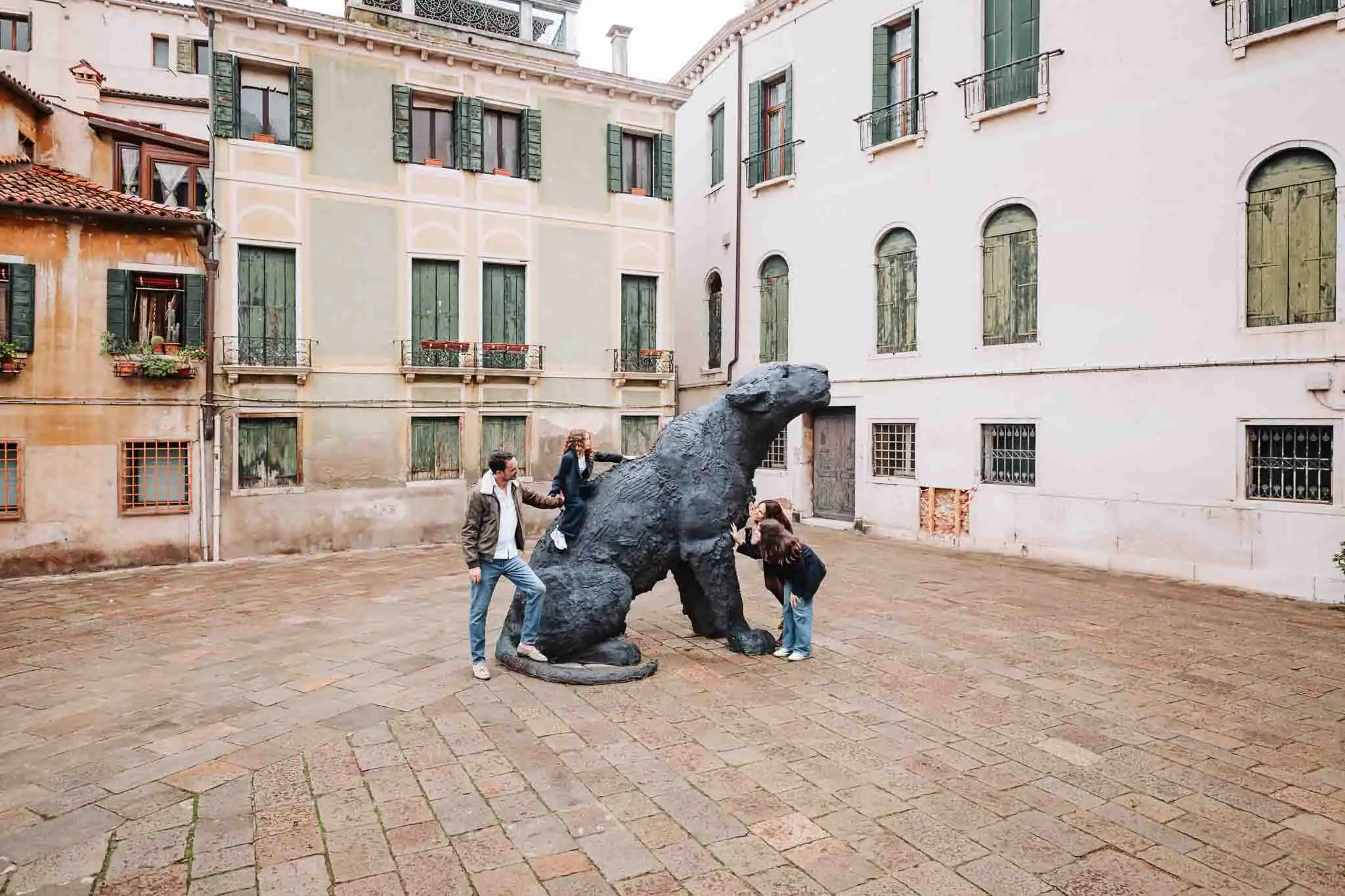 1. Children playing on a dinosaur sculpture in a Venice courtyard with colorful old buildings.
