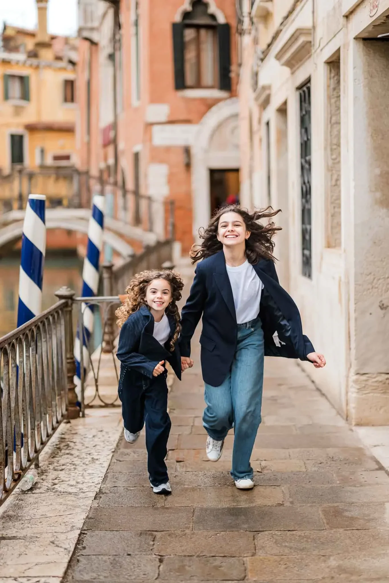 1. Smiling woman and girl running in Venice street with colorful historic buildings behind.