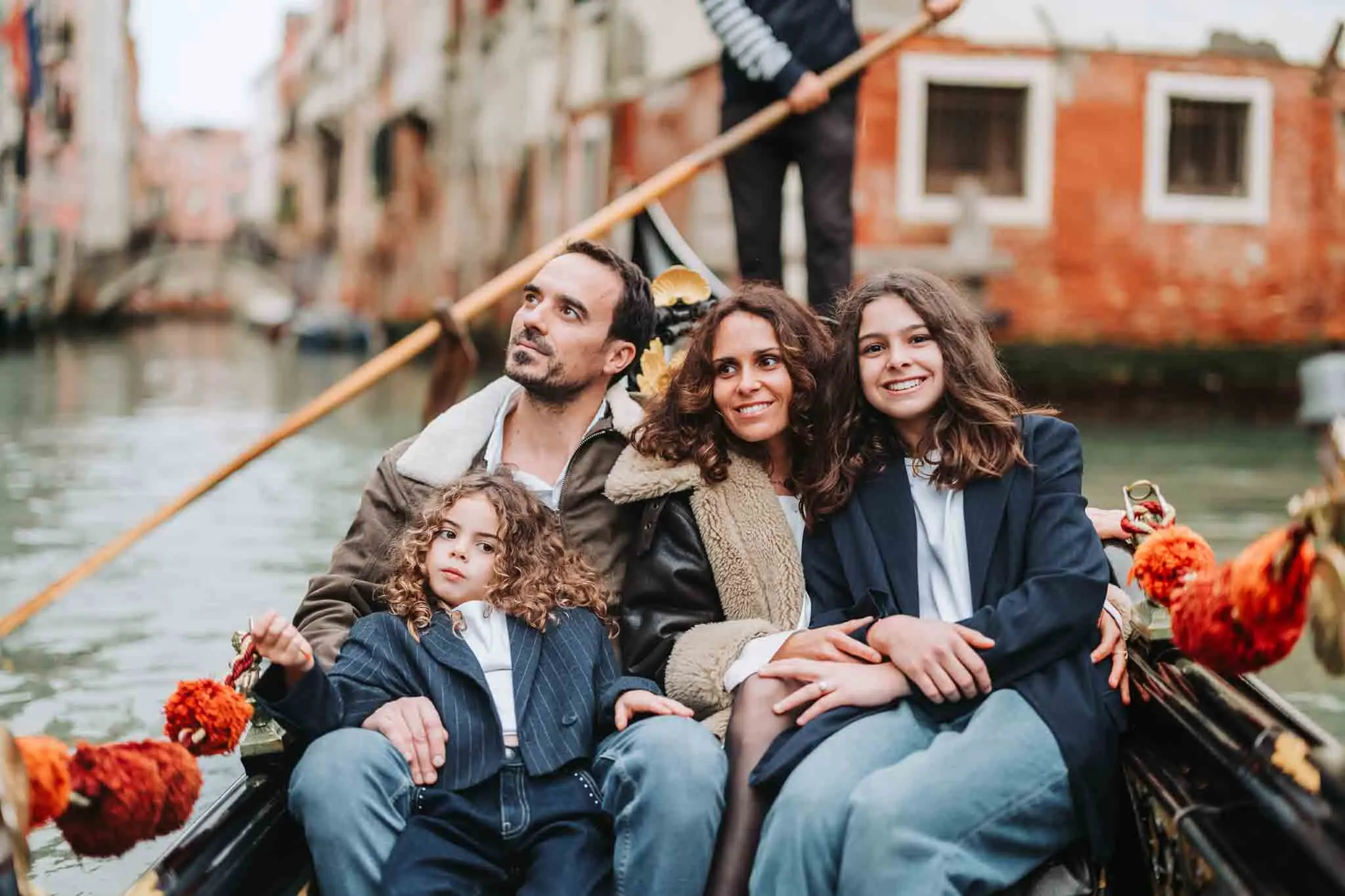 Venezia family gondola ride with smiling parents and children, scenic canal backdrop, candid moment.