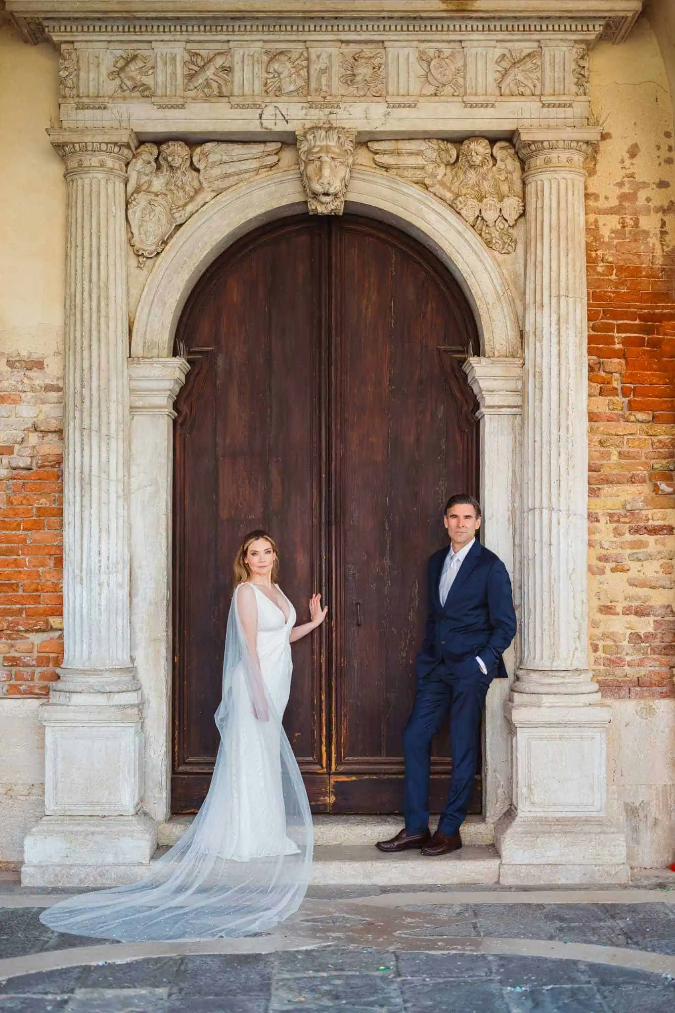 Elegant bride and groom in wedding attire posing against historic Venetian door, showcasing romance and architecture.