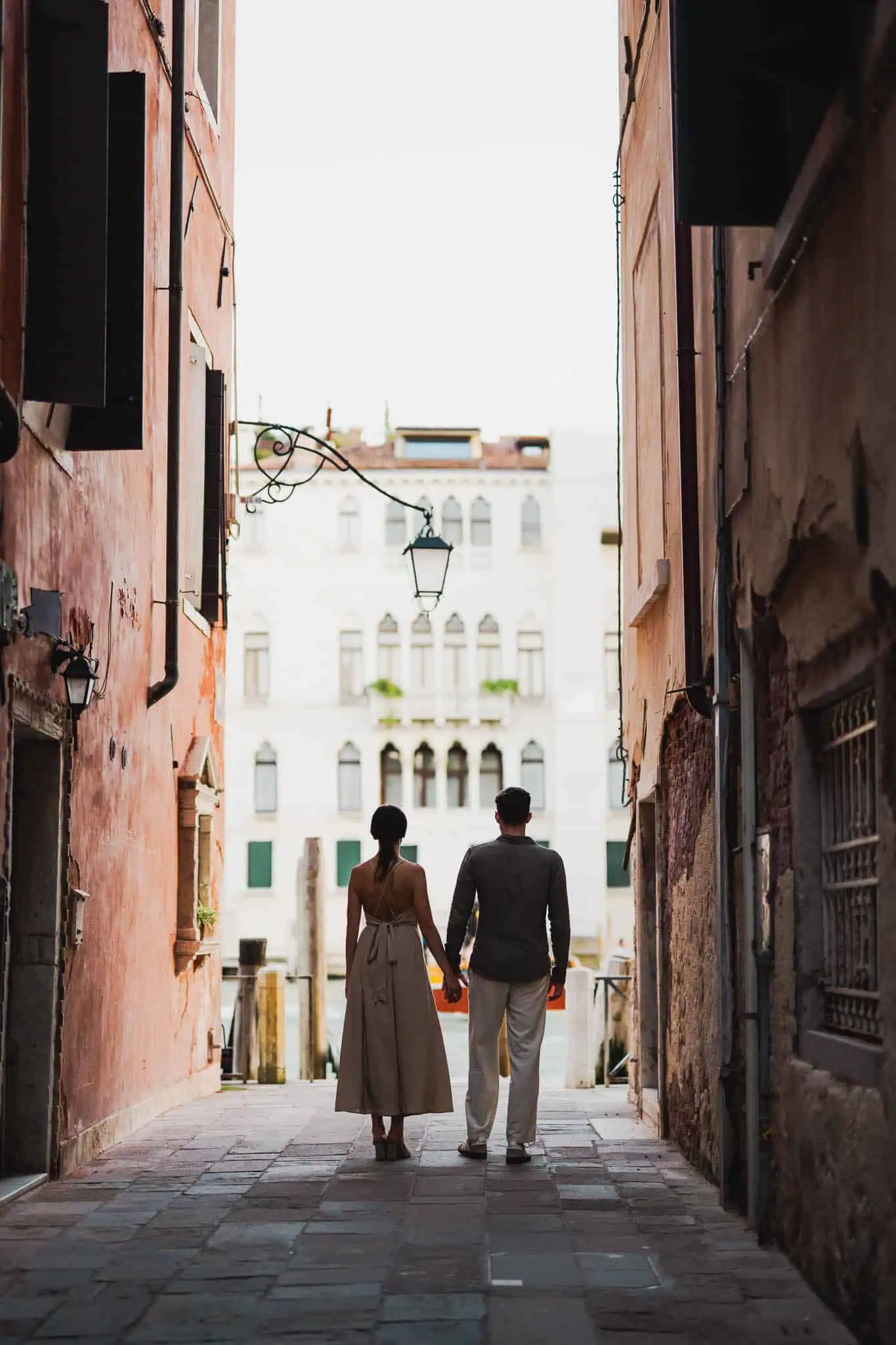 1. Couple holding hands walking through a narrow Venetian alleyway during sunset.