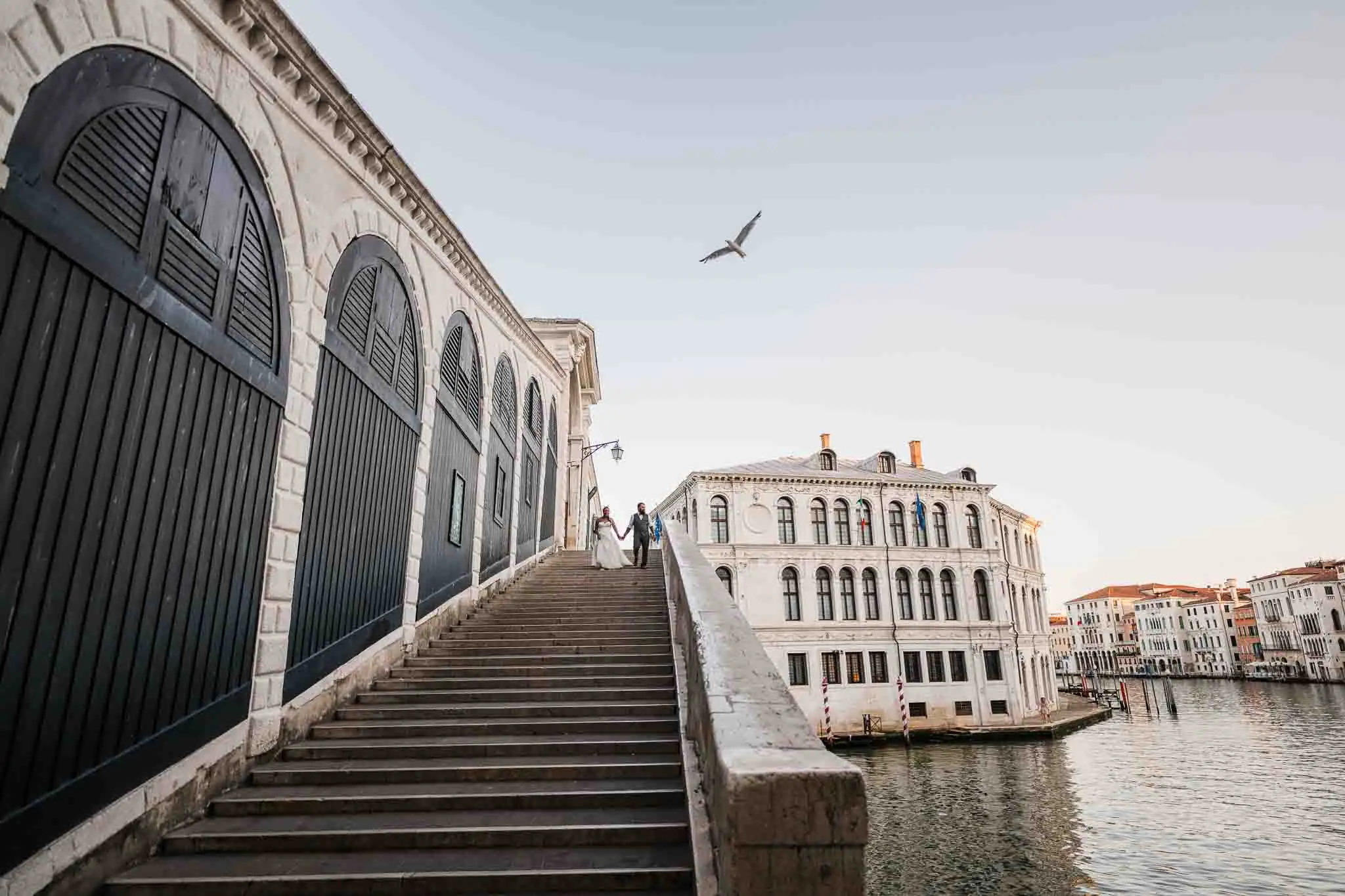 Elegant Venice wedding couple holding hands on historic staircase by canal at sunset.