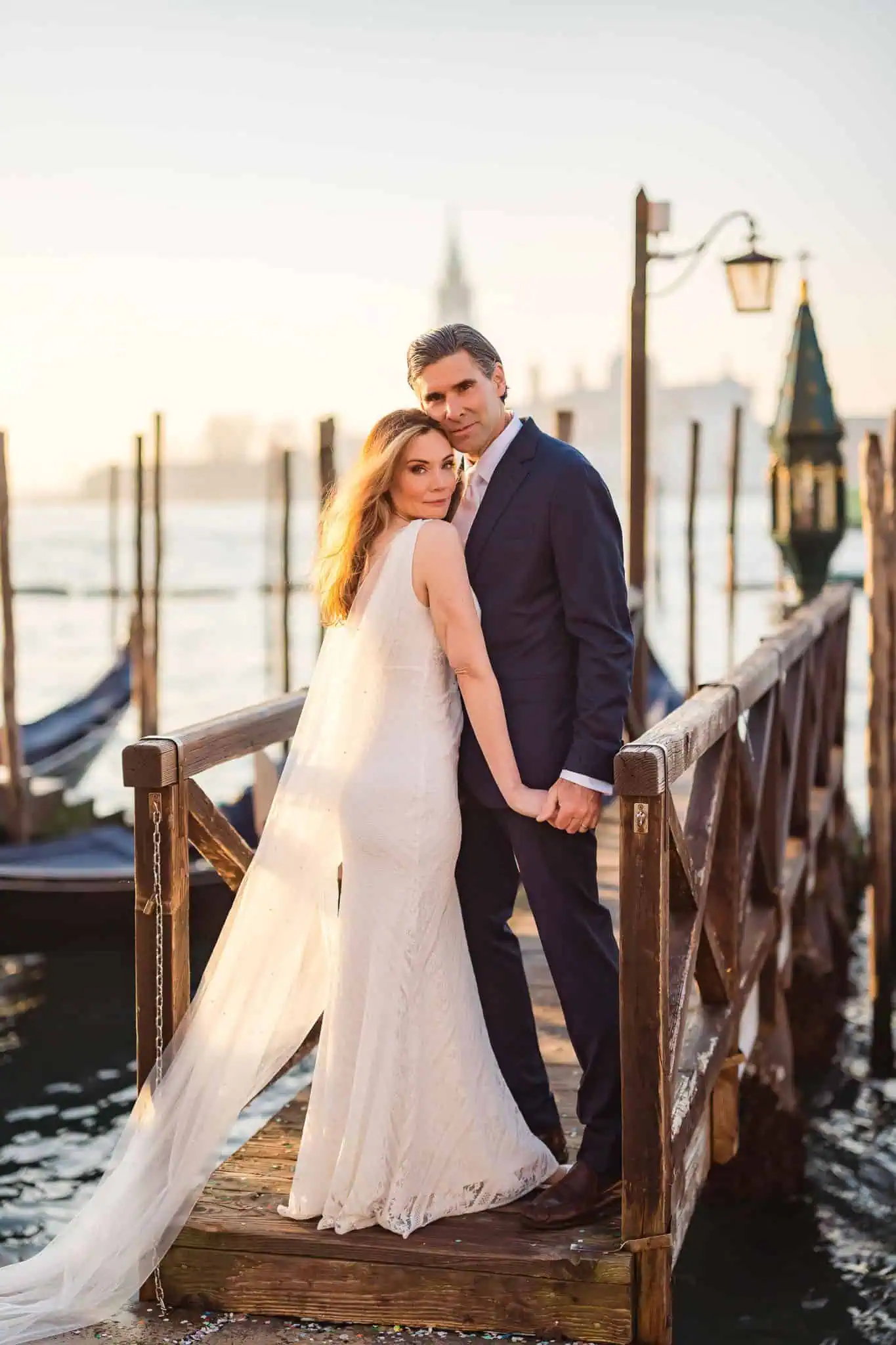 Elegant couple in wedding attire on a Venice pier during sunset, capturing romantic engagement moments.