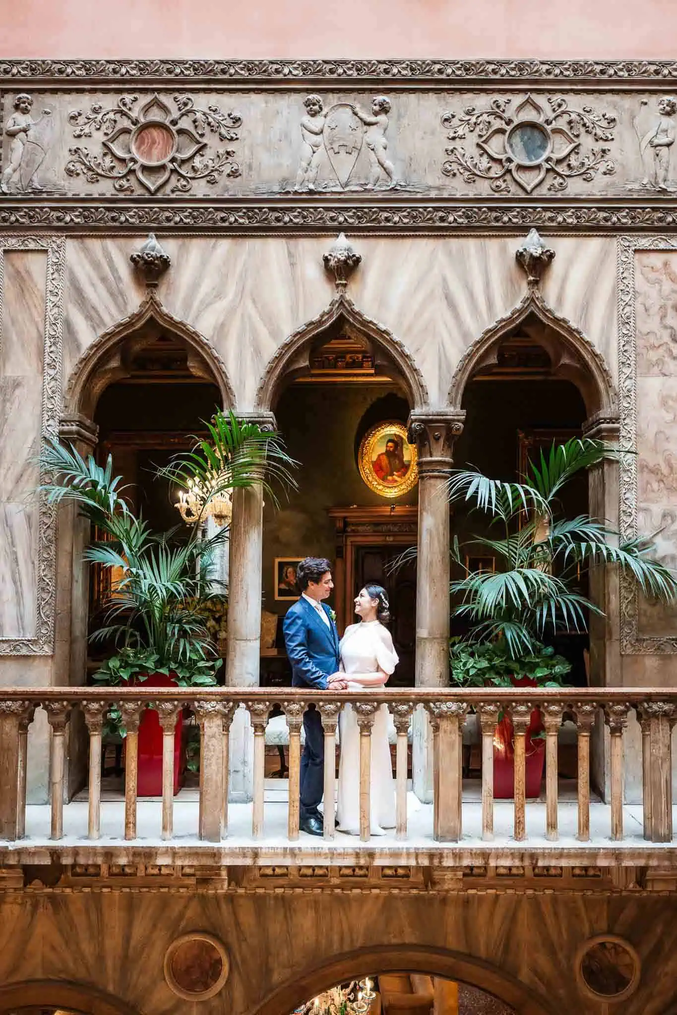 1. Elegant couple holding hands on ornate Venetian balcony with historic architecture.