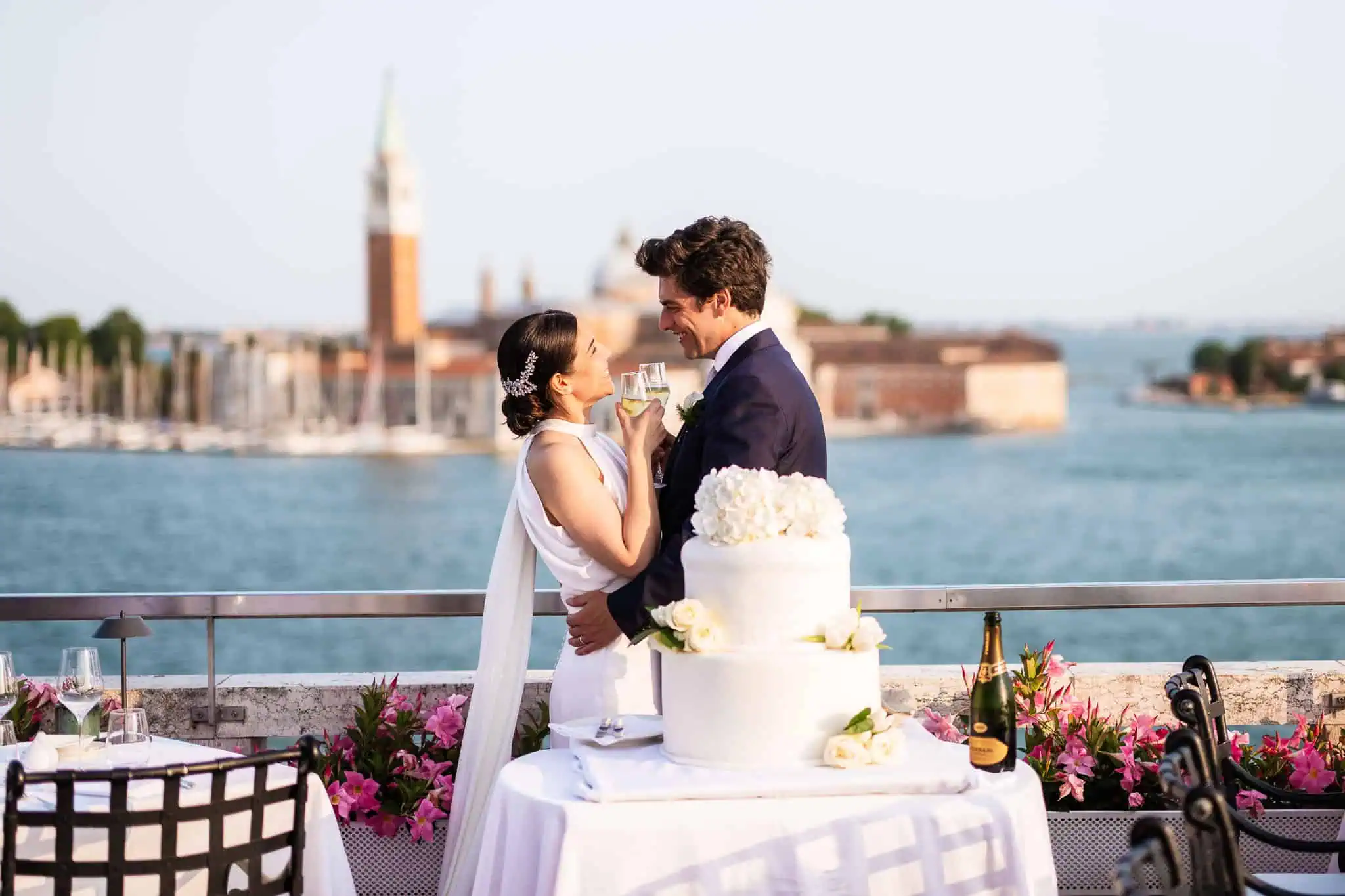 Romantic Venice wedding celebration with couple holding glasses, iconic city background, and elegant cake.