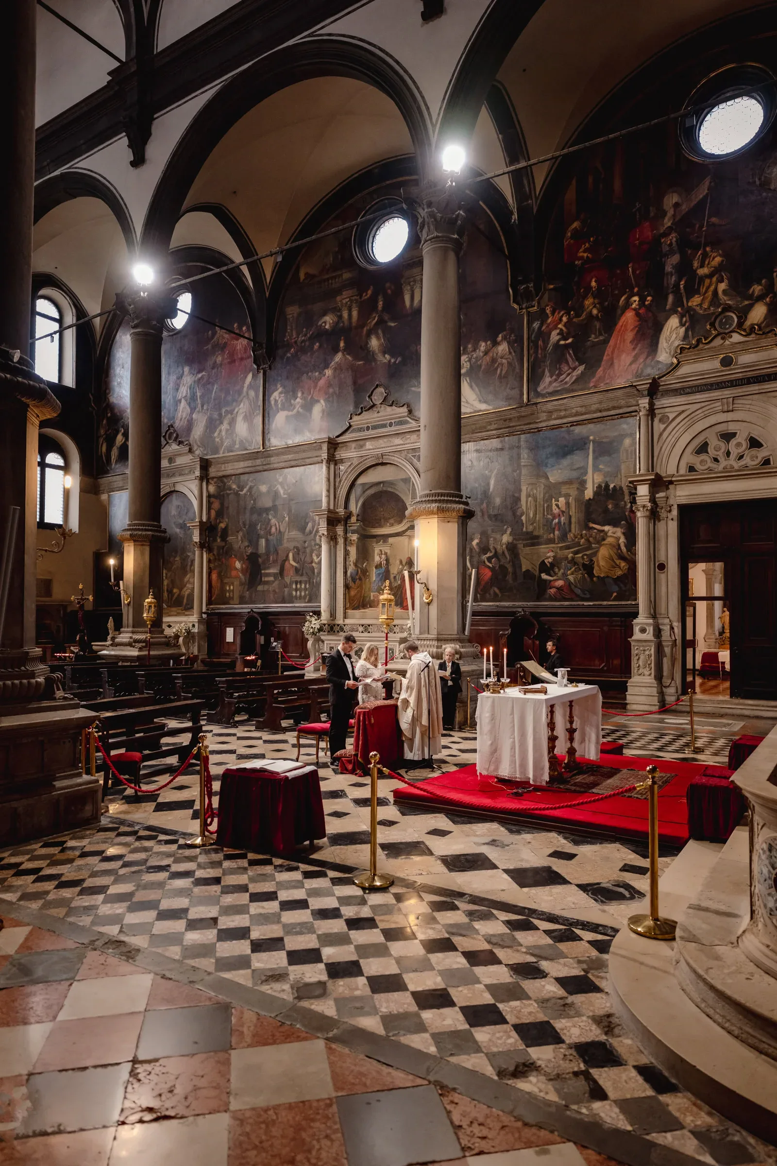 Elegant couple ceremony taking place inside a historic church with large wall murals and classical architecture.
