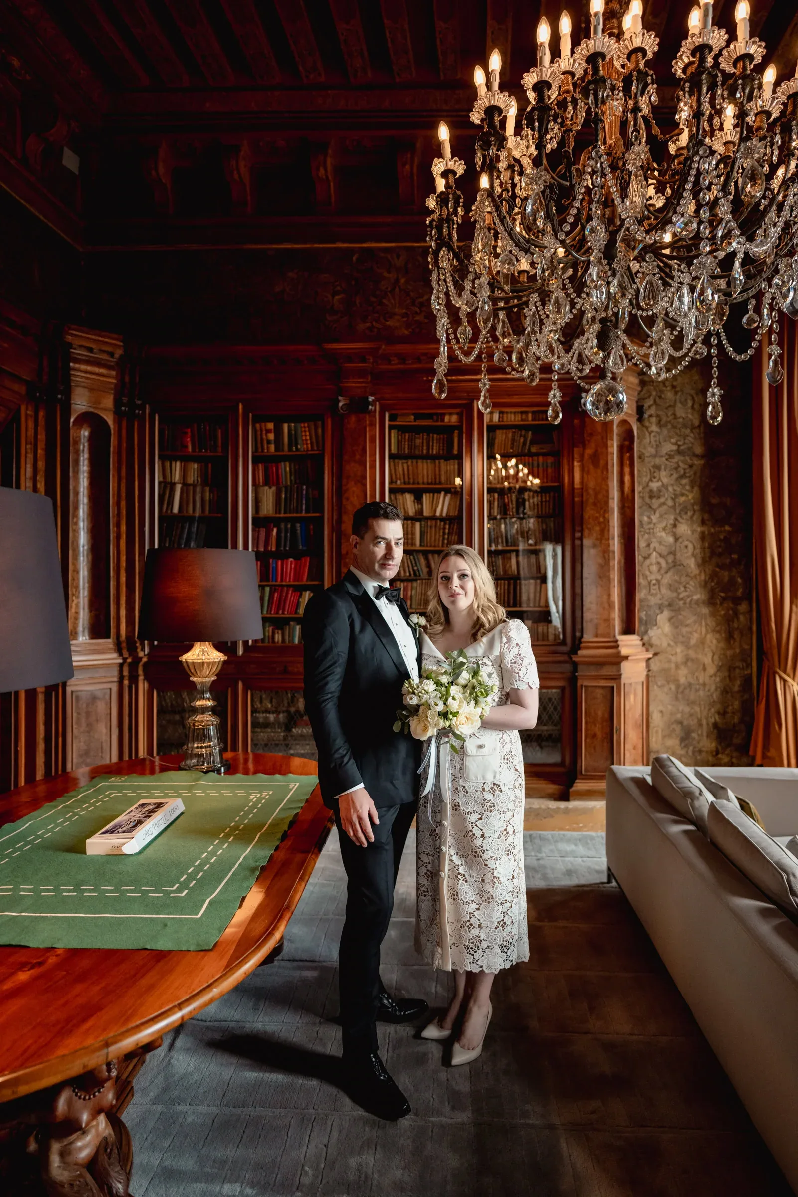 Elegant couple in formal attire standing in luxurious library during intimate elopement ceremony.