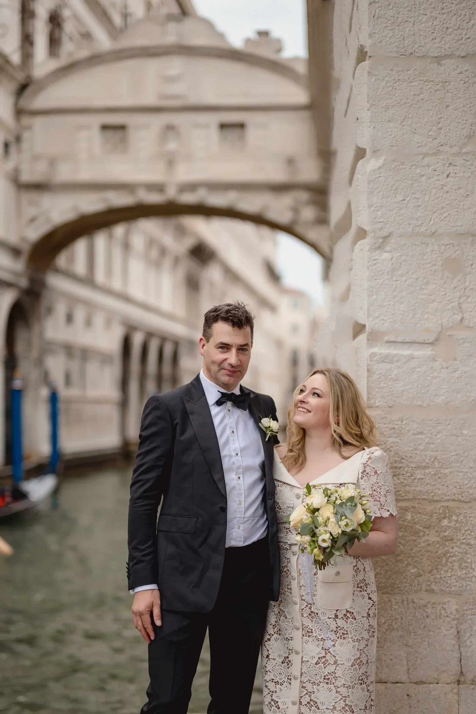 Elegant couple standing beside a canal in Venice.