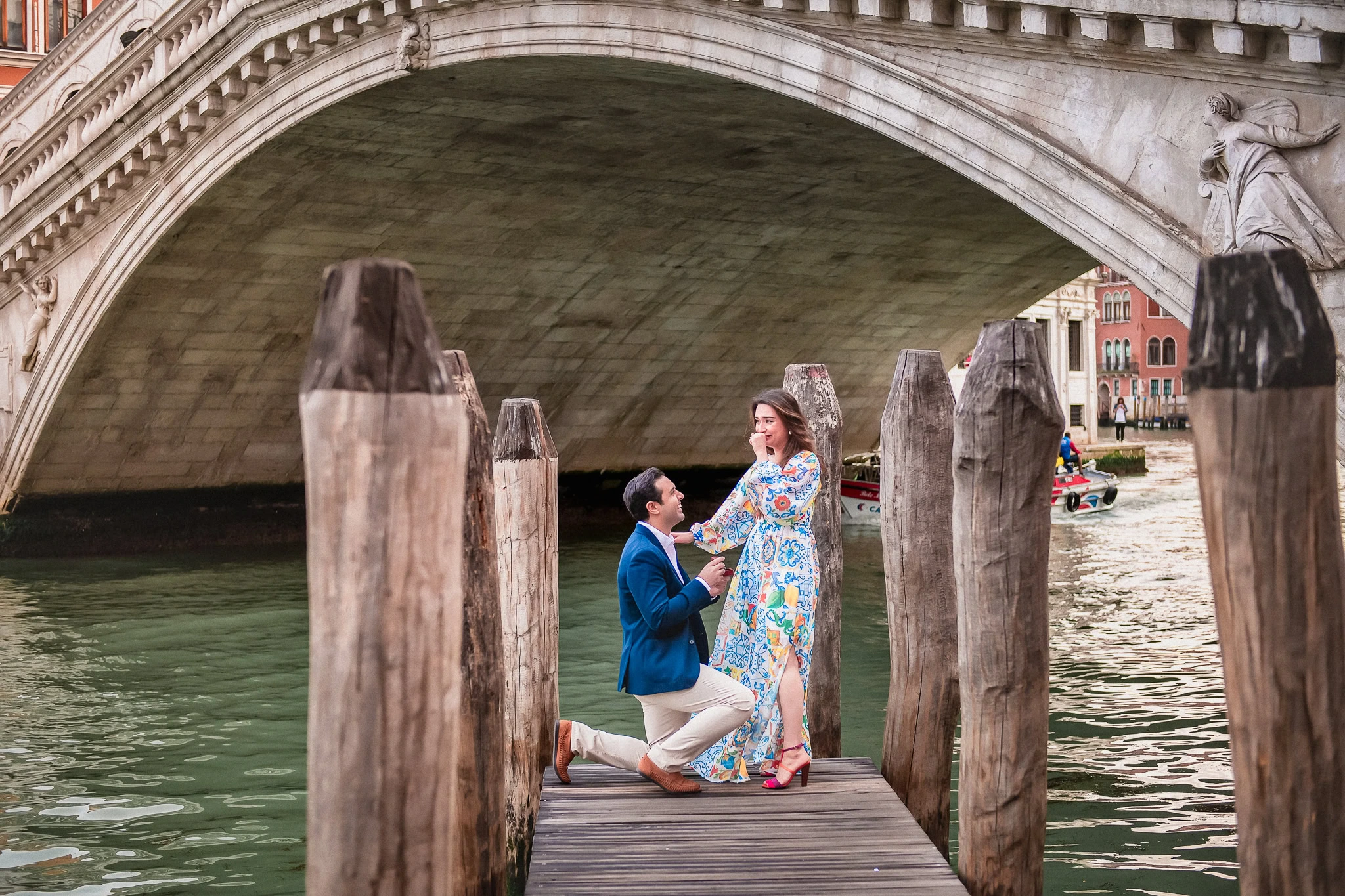 Romantic proposal under Venice's historic bridge with gondola in background.
