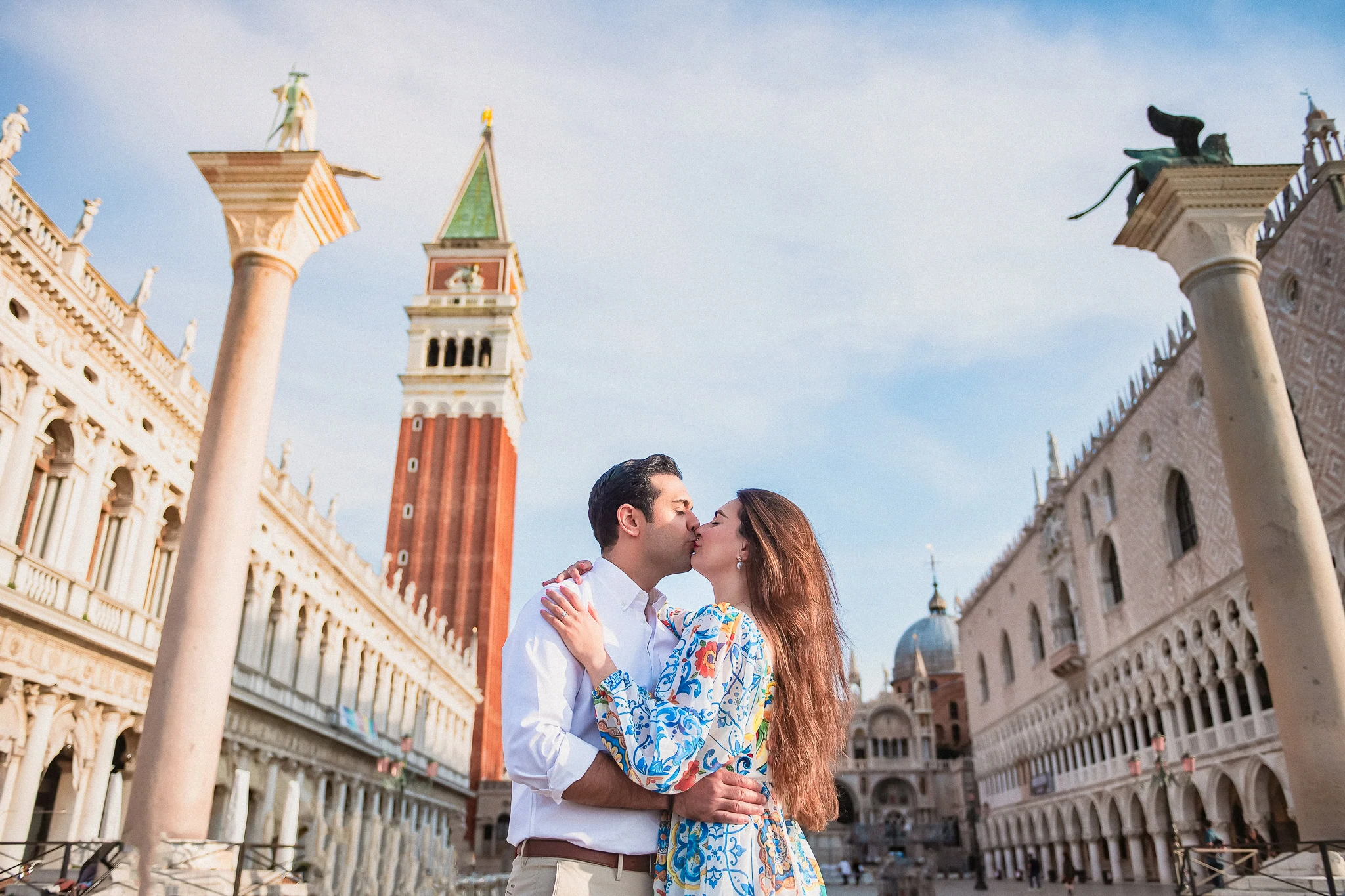 Romantic couple kissing at St. Mark's Square, Venice, with historic architecture and iconic bell tower in background.