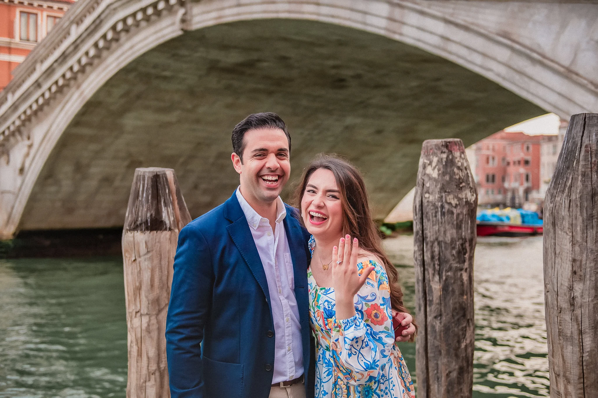 Beautiful couple celebrating engagement near Venice canal, with iconic bridge in the background.