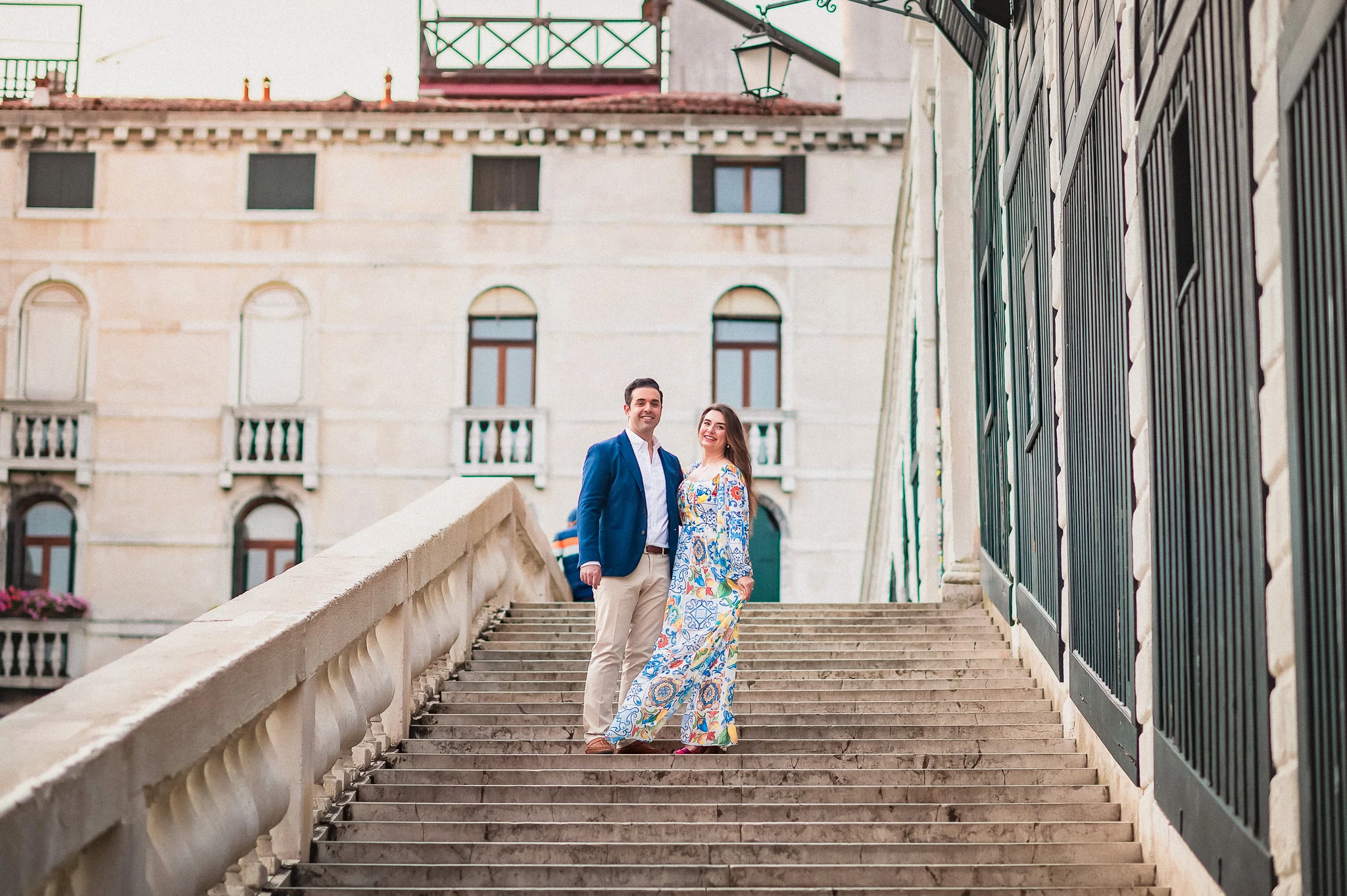 Elegant couple on Venetian stairs in colorful summer attire, romantic engagement photo in Venice.
