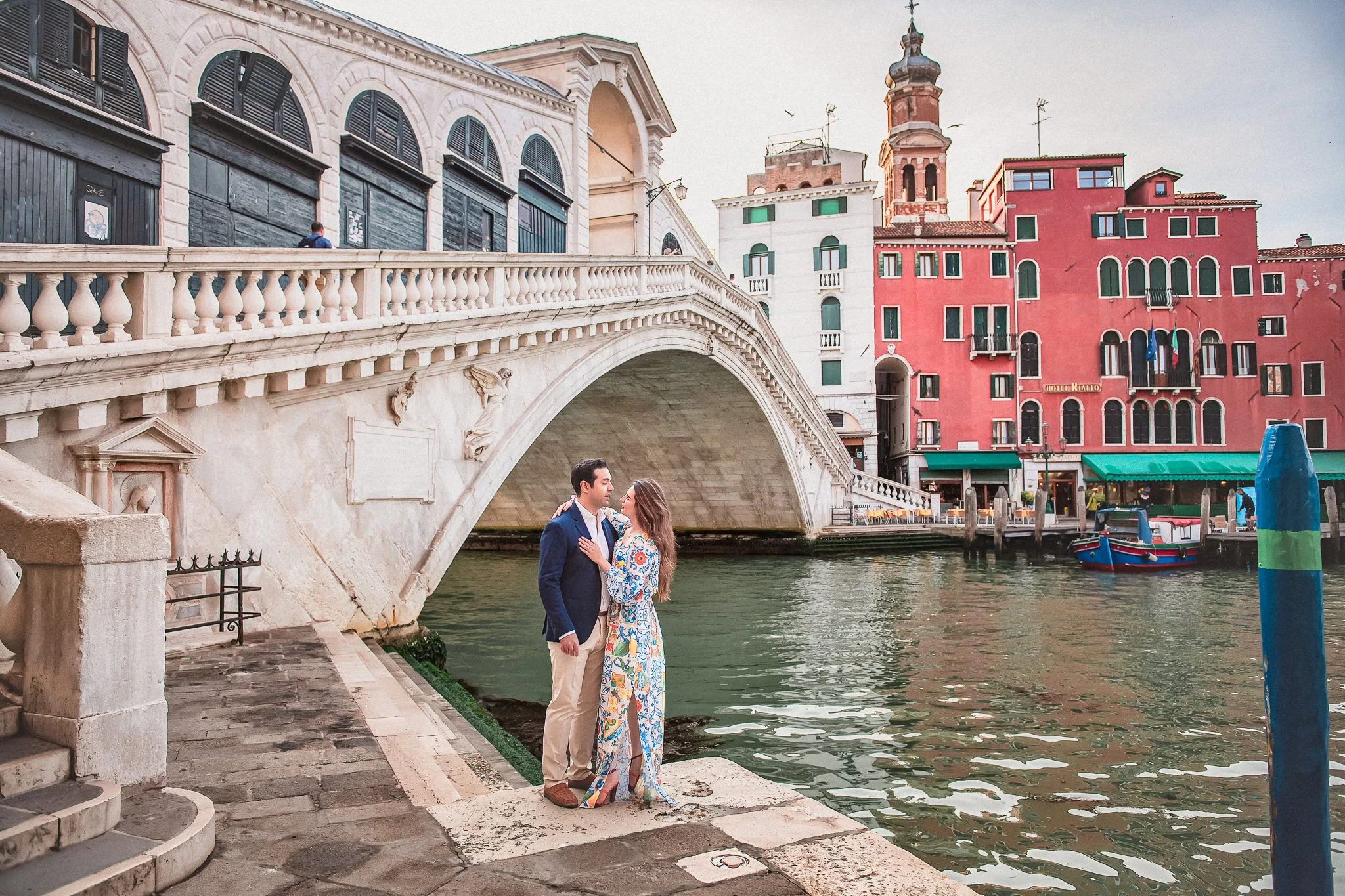 Romantic couple in Venice by canal, engagement photoshoot, cityscape, colorful buildings in background.