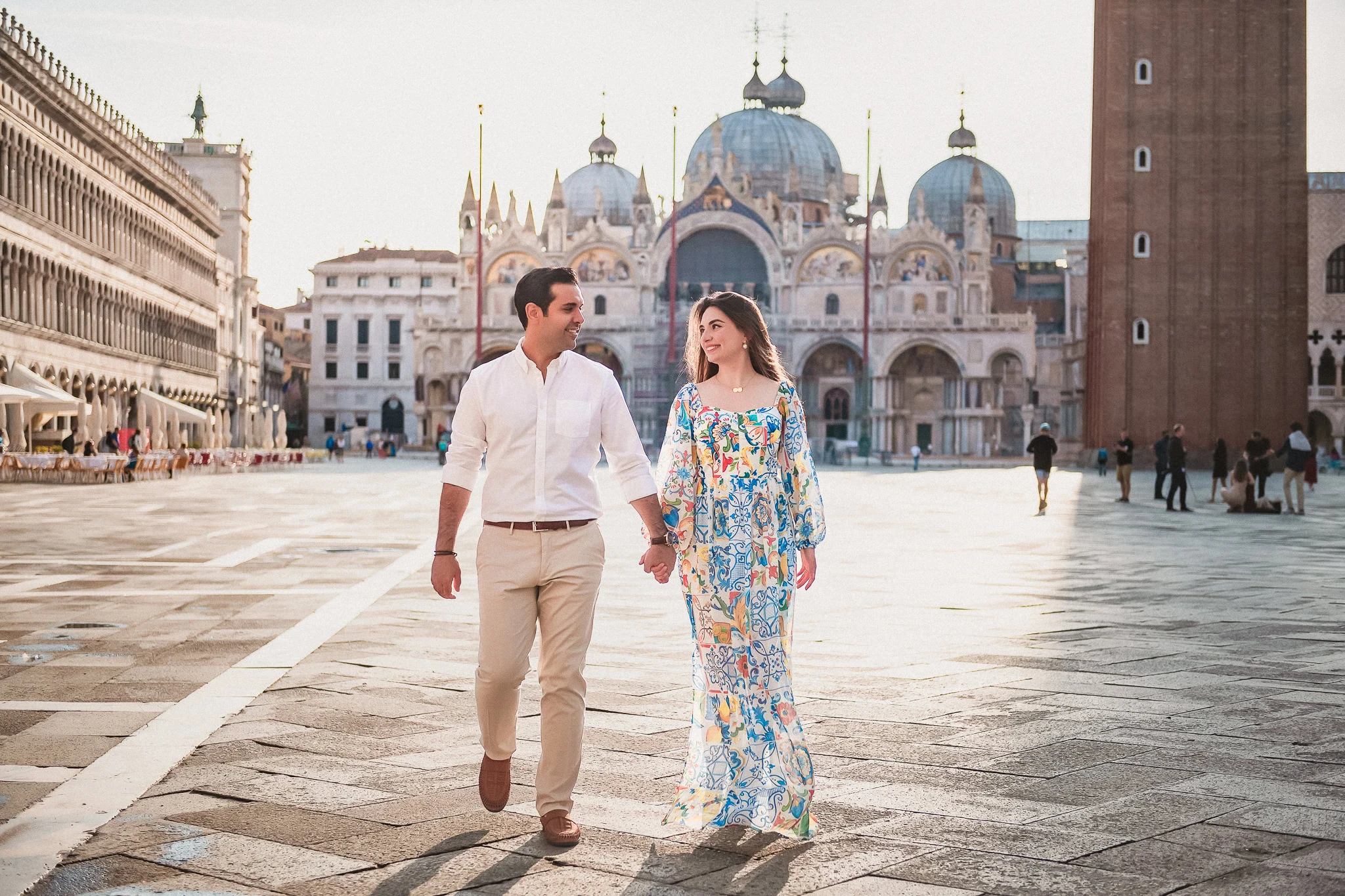 Romantic Venice couple walking hand in hand in Piazza San Marco at sunset, celebrating love and engagement.