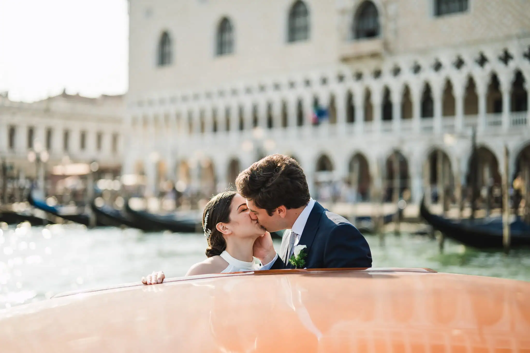 Romantic couple kissing in a gondola on Venice canals during their wedding photoshoot.