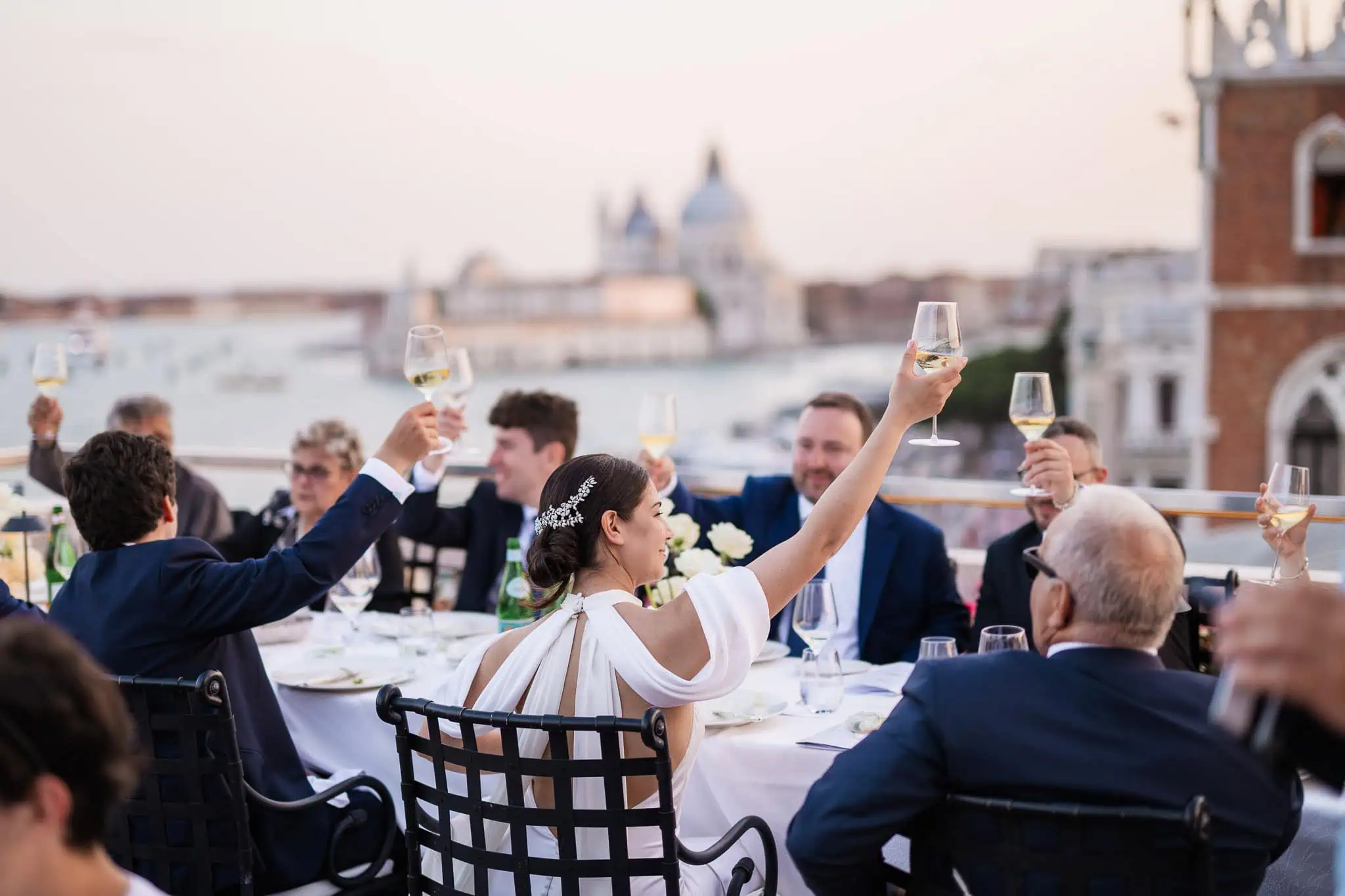 Elegant bride and guests celebrate with champagne on a rooftop in Venice at a wedding reception.