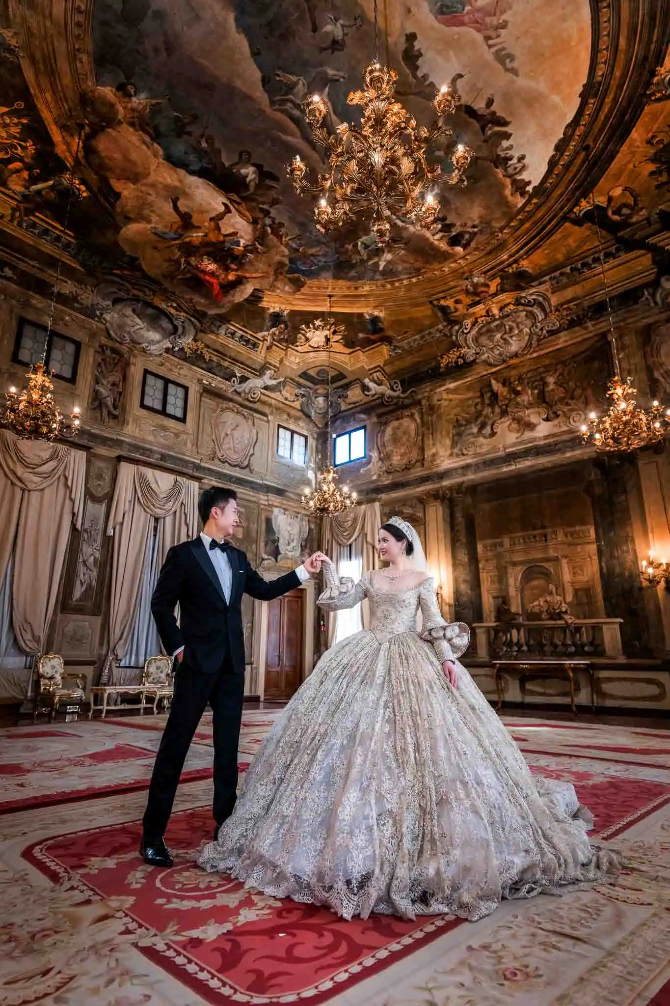 Elegant wedding couple dancing in ornate Venetian palace with grand chandeliers and historical interior.