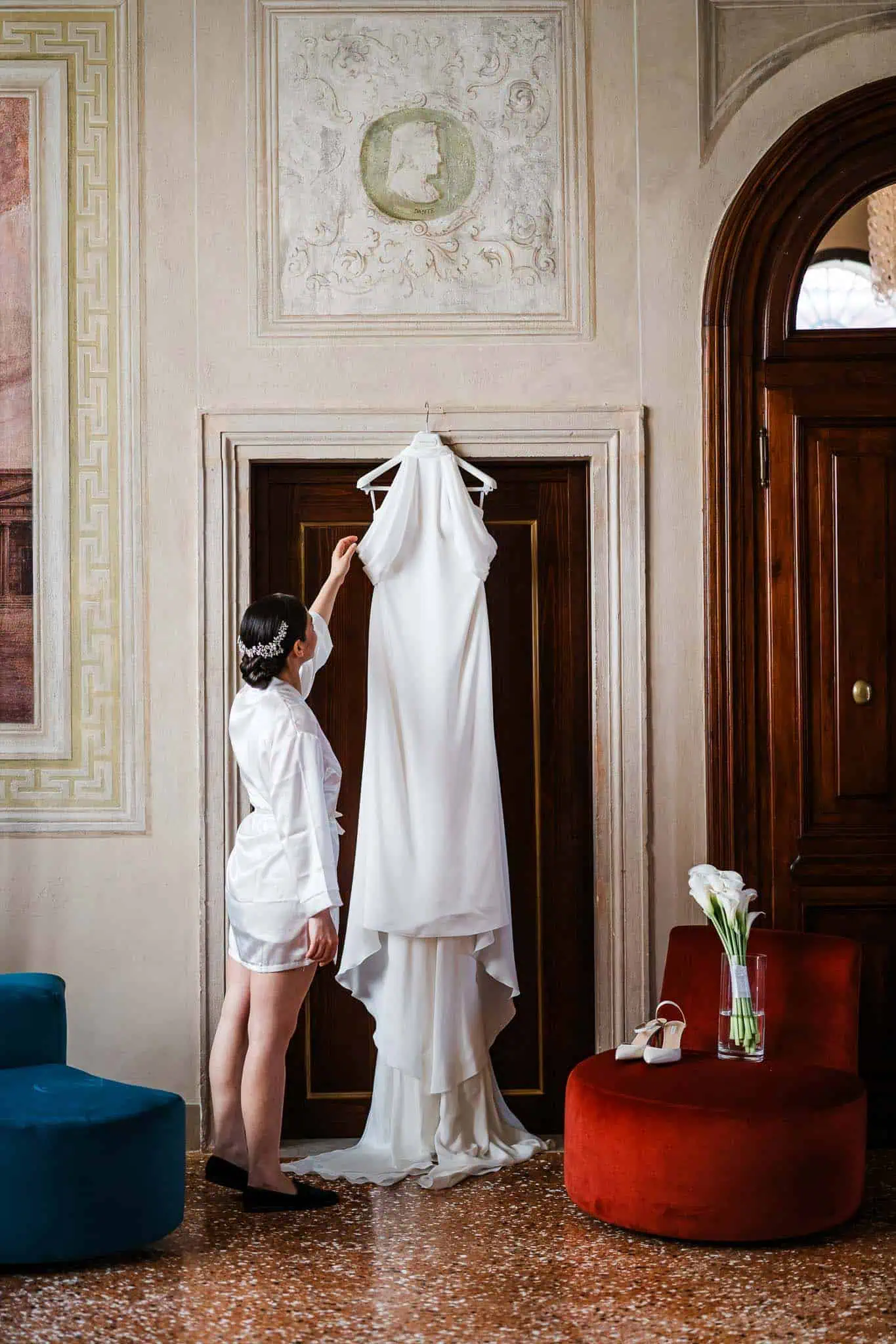 Elegant bride preparing for wedding day in Venice, holding white wedding dress with vintage decor.
