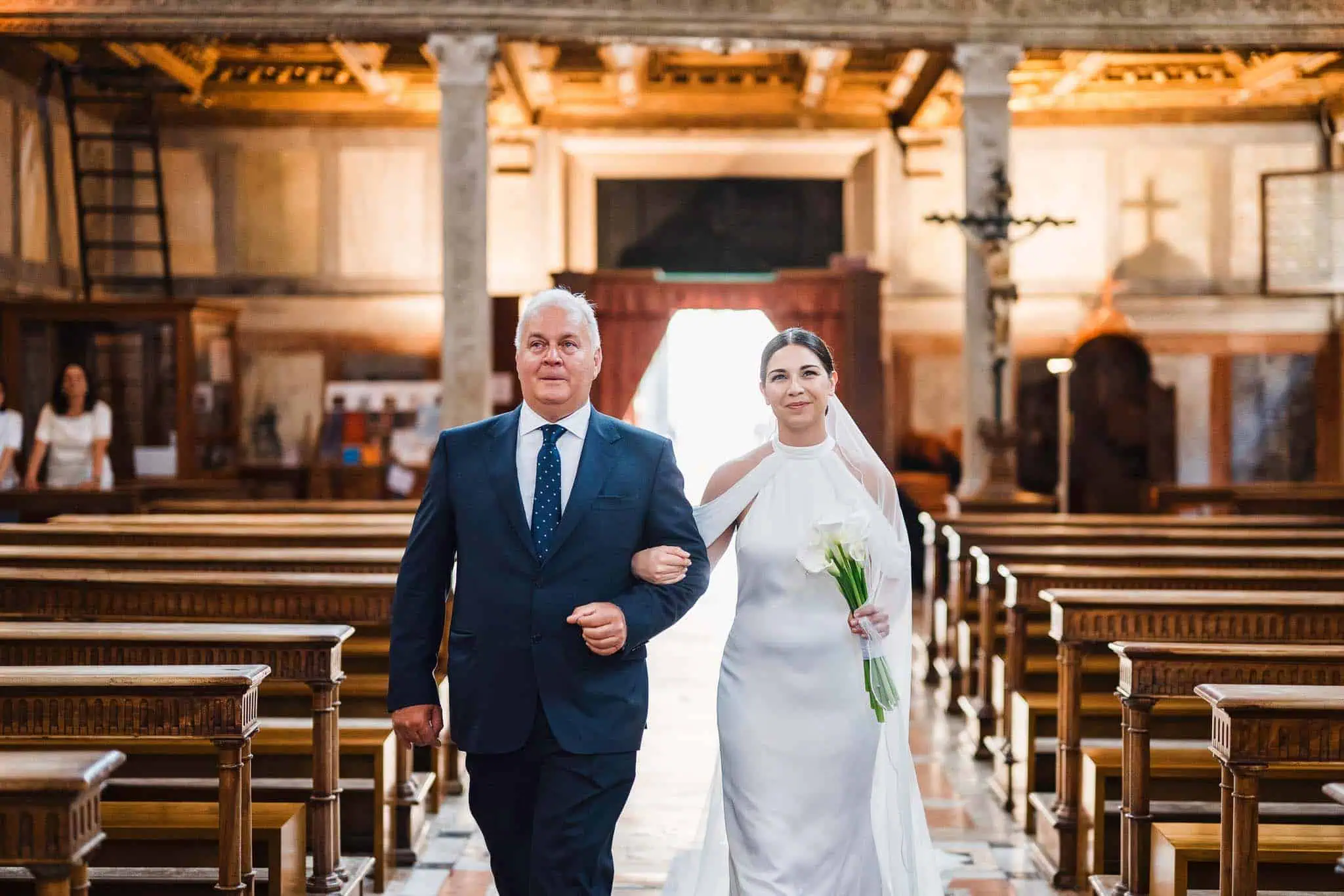 Elegant bride walking down the aisle with her father in a historic church in Venice.