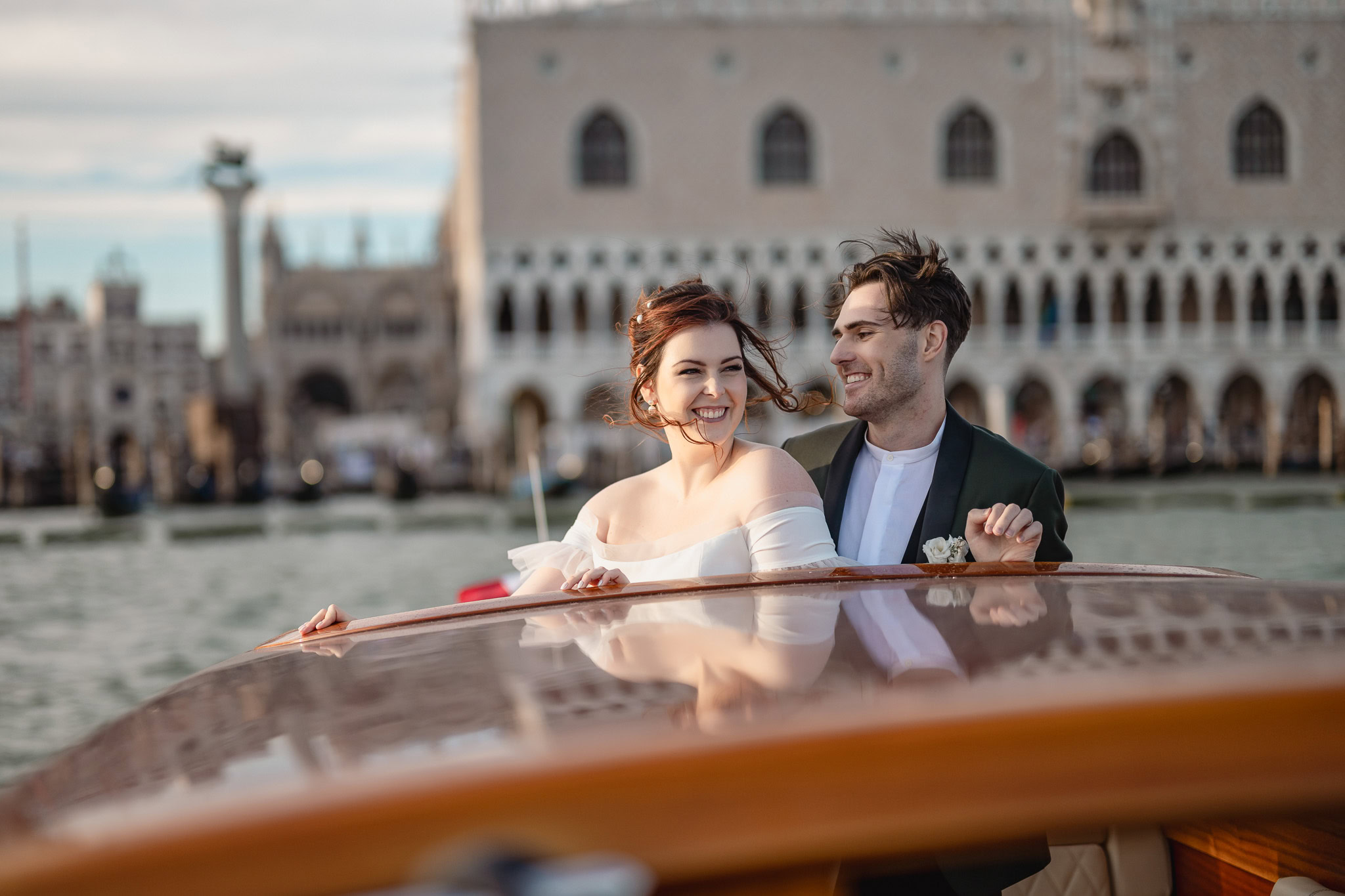 Couple smiling on a boat with Ca’ Sagredo Palace in Venice in the background.