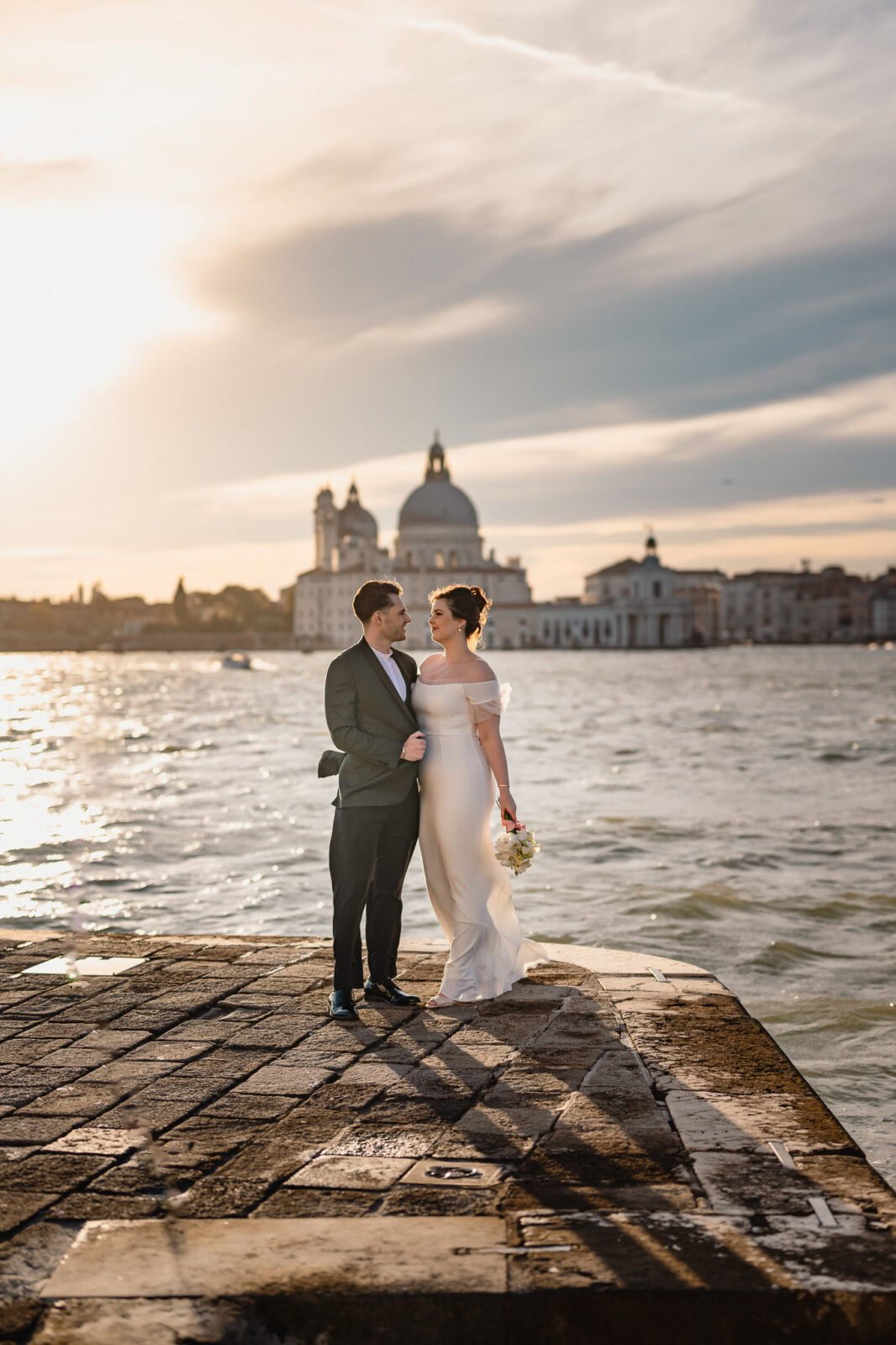 Couple standing on a stone dock by the water with Ca’ Sagredo Palace in the background dur.