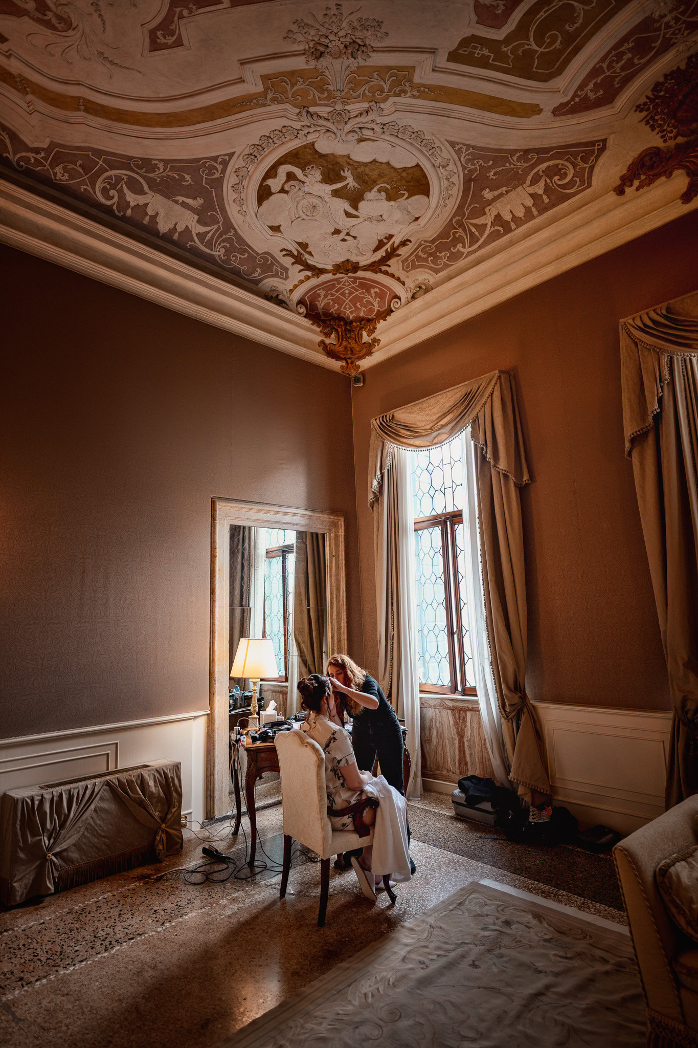 A couple sitting in an elegant room at Ca’ Sagredo Palace, with ornate ceiling details and.
